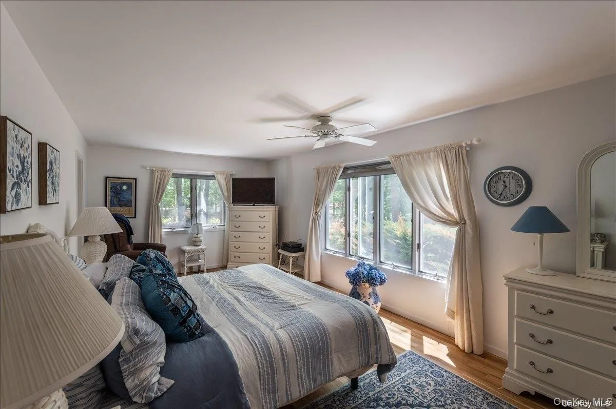 Bright bedroom featuring multiple windows, a ceiling fan with integrated lighting, and wood-finish flooring Bright bedroom featuring multiple windows, a ceiling fan with integrated lighting, and wood-finish flooring