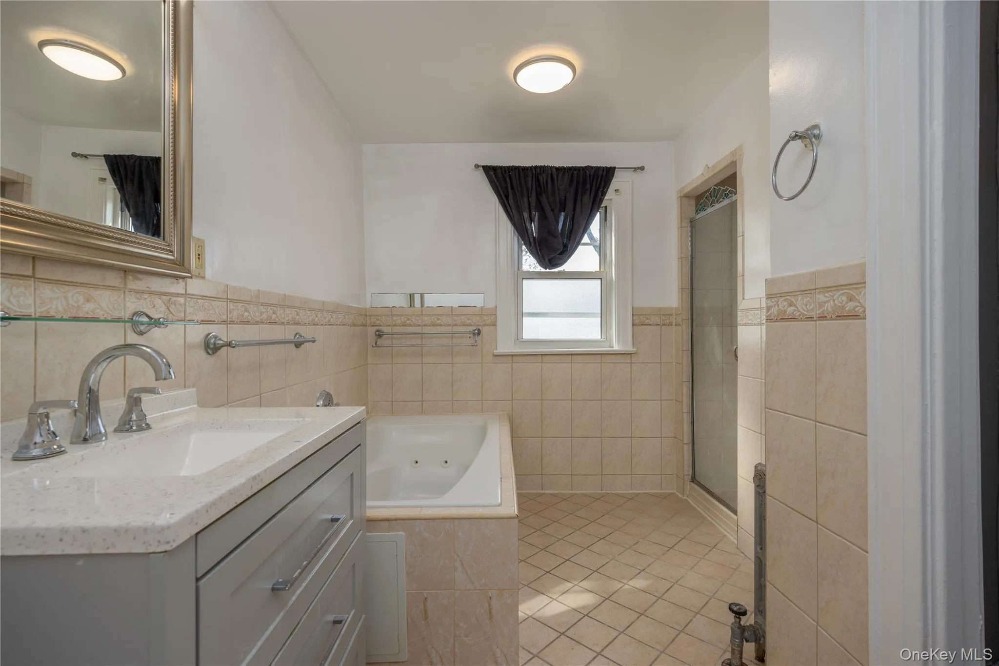 Primary Bathroom featuring a light gray vanity with three drawers, an integrated sink, coordinating countertop, chrome fixtures, a jetted tub, and a glass-enclosed shower Primary Bathroom featuring a light gray vanity with three drawers, an integrated sink, coordinating countertop, chrome fixtures, a jetted tub, and a glass-enclosed shower