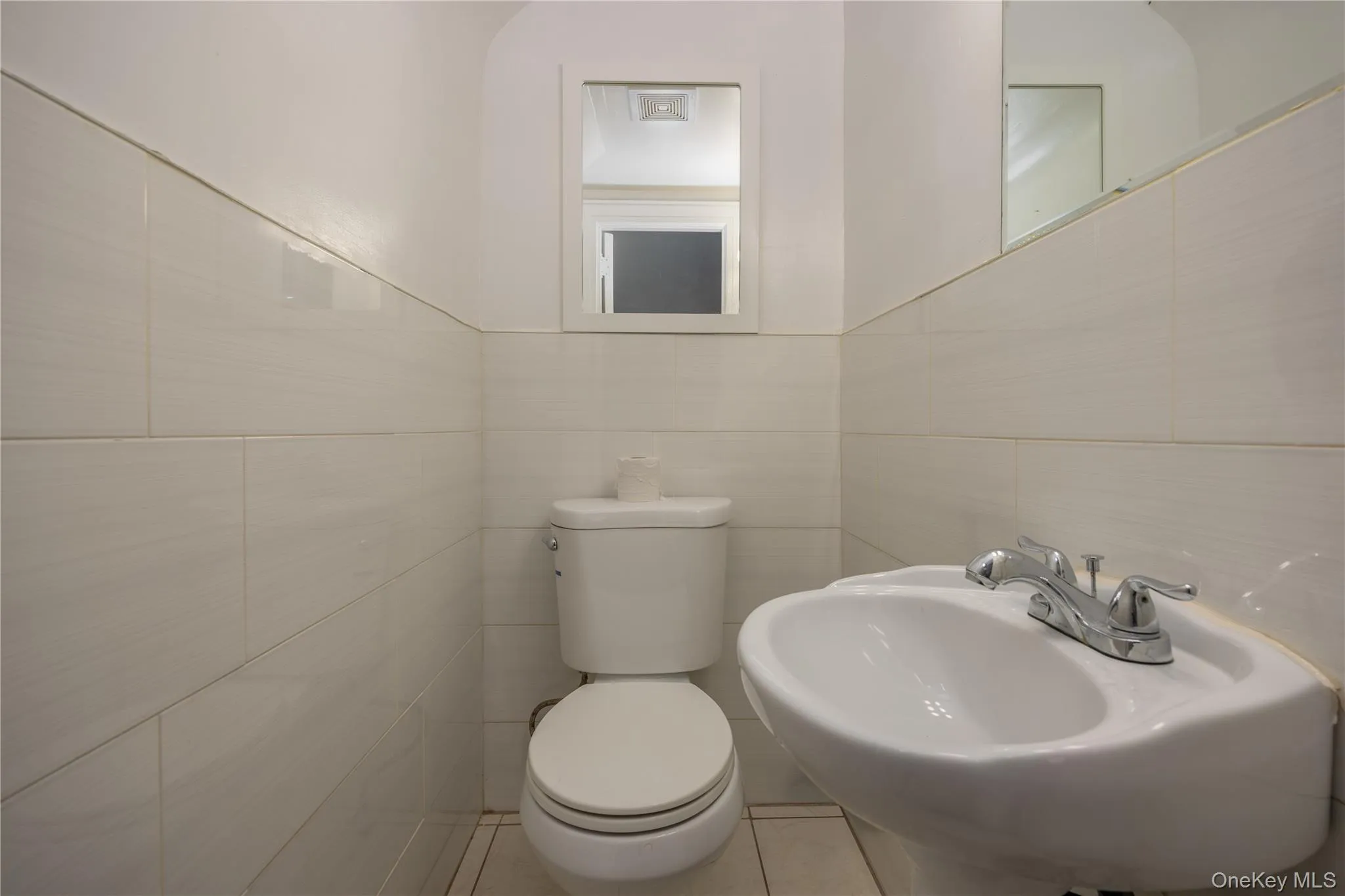 First floor half Bathroom featuring a wall-mounted sink, a toilet, and ceramic wall tiling First floor half Bathroom featuring a wall-mounted sink, a toilet, and ceramic wall tiling