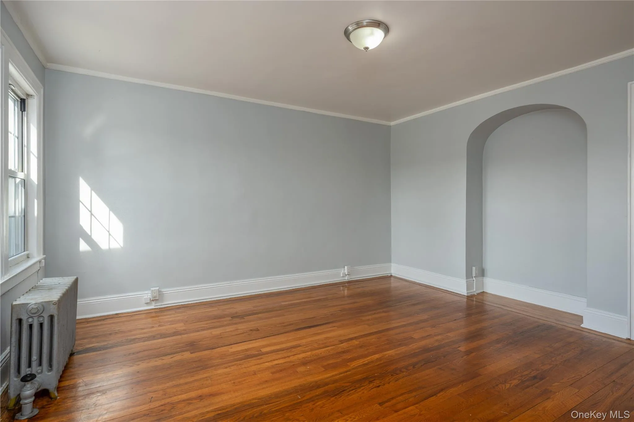 Primary Bedroom12'3" × 13'6" featuring wood-finish flooring, a double-hung window, and an arched wall niche Primary Bedroom12'3" × 13'6" featuring wood-finish flooring, a double-hung window, and an arched wall niche