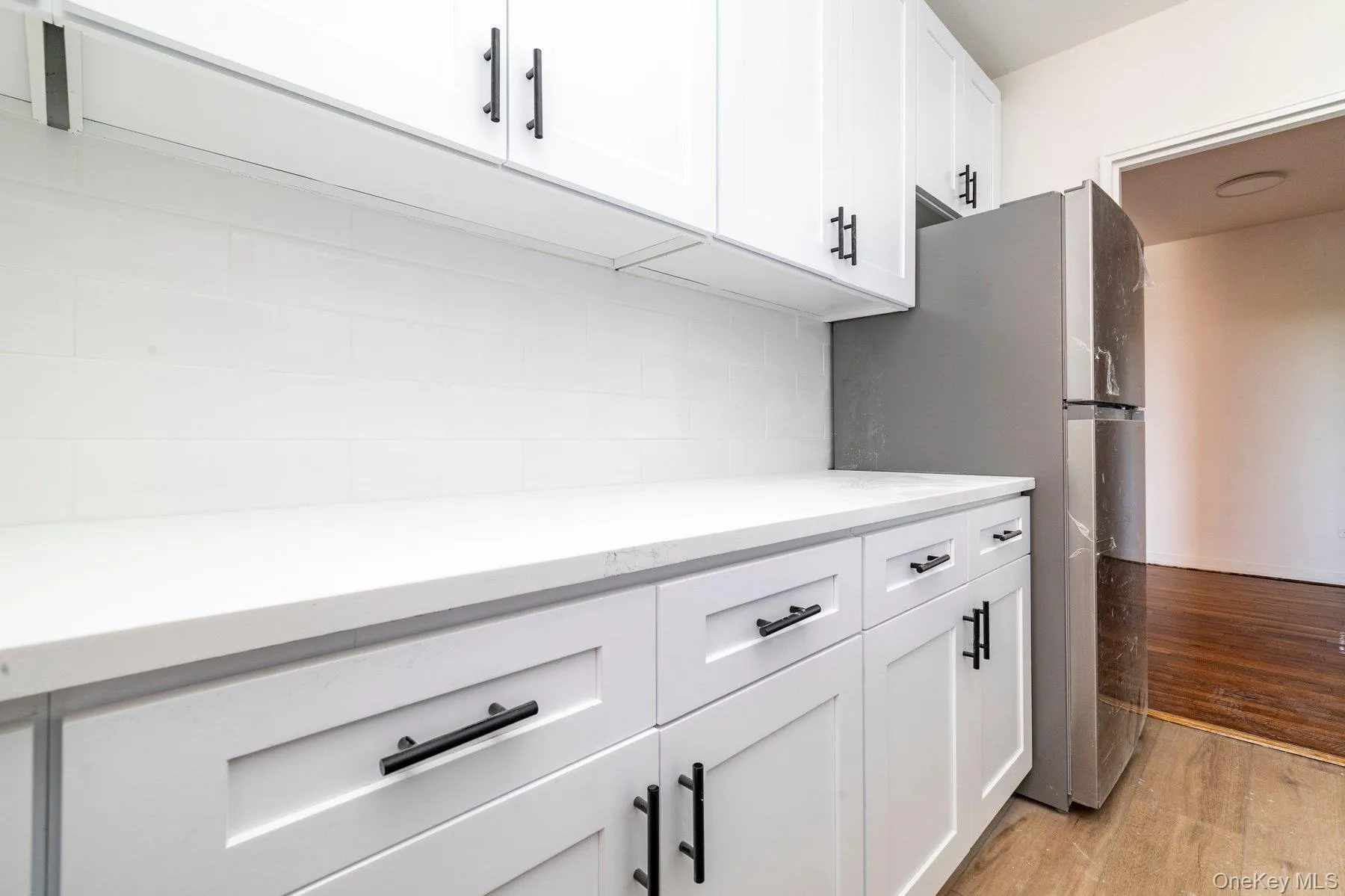 Modern kitchen featuring white shaker cabinetry with matte black hardware, white countertops, and a subway tile backsplash Modern kitchen featuring white shaker cabinetry with matte black hardware, white countertops, and a subway tile backsplash