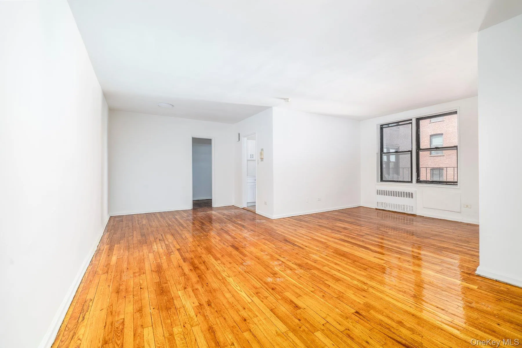 Expansive living area featuring wood-finish flooring, white walls, and a large multi-pane window Expansive living area featuring wood-finish flooring, white walls, and a large multi-pane window