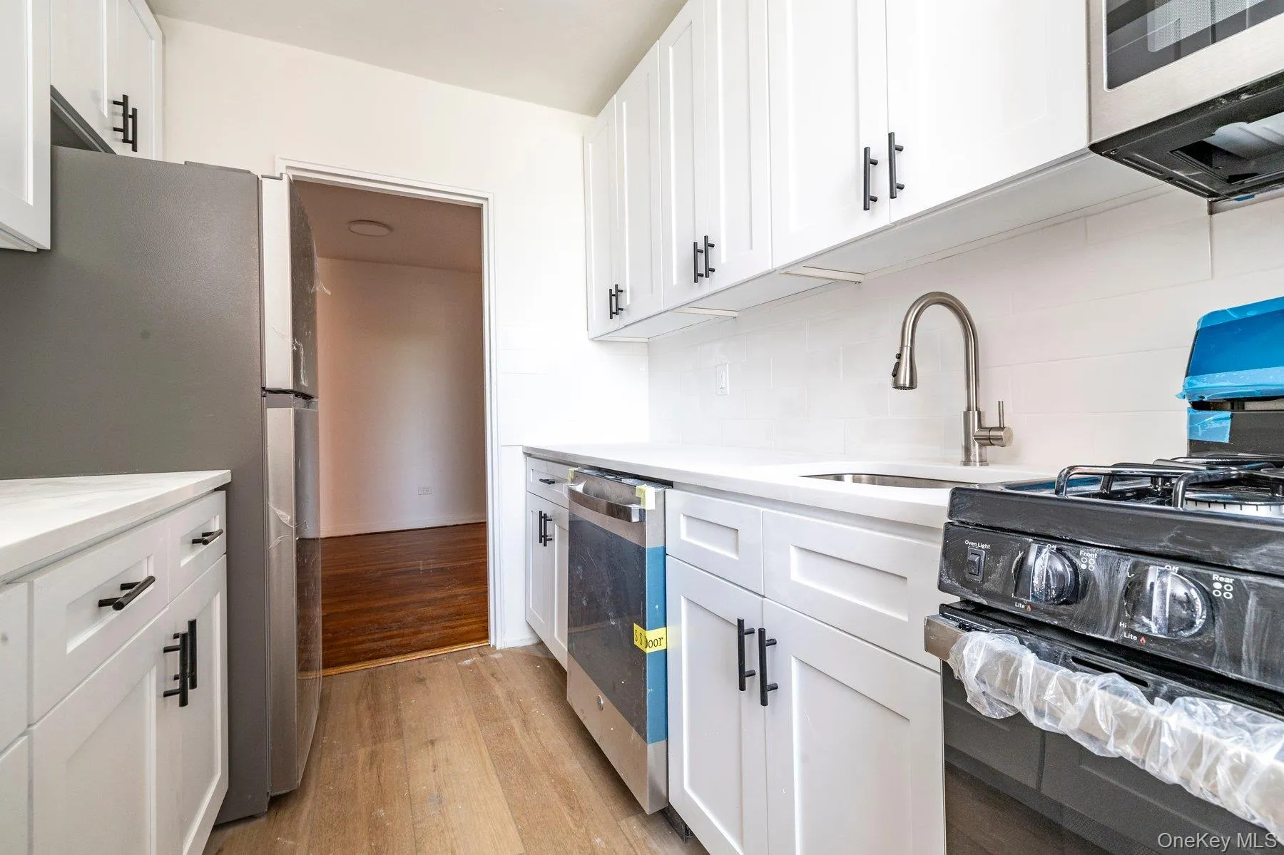 Modern kitchen featuring white shaker cabinetry with black hardware, white countertops, subway tile backsplash, and stainless steel appliances Modern kitchen featuring white shaker cabinetry with black hardware, white countertops, subway tile backsplash, and stainless steel appliances