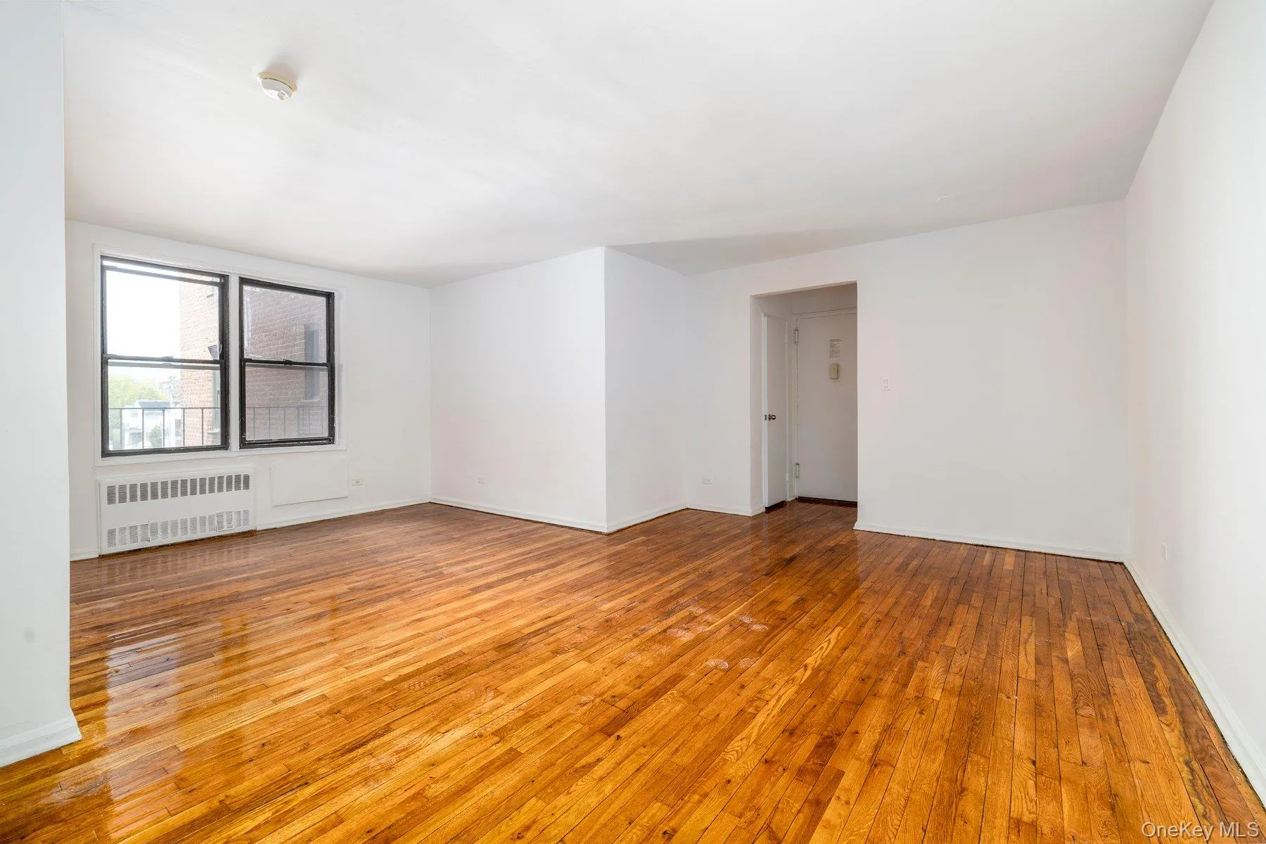 Living space featuring wood-finish flooring, white walls, and a large window with black framing Living space featuring wood-finish flooring, white walls, and a large window with black framing