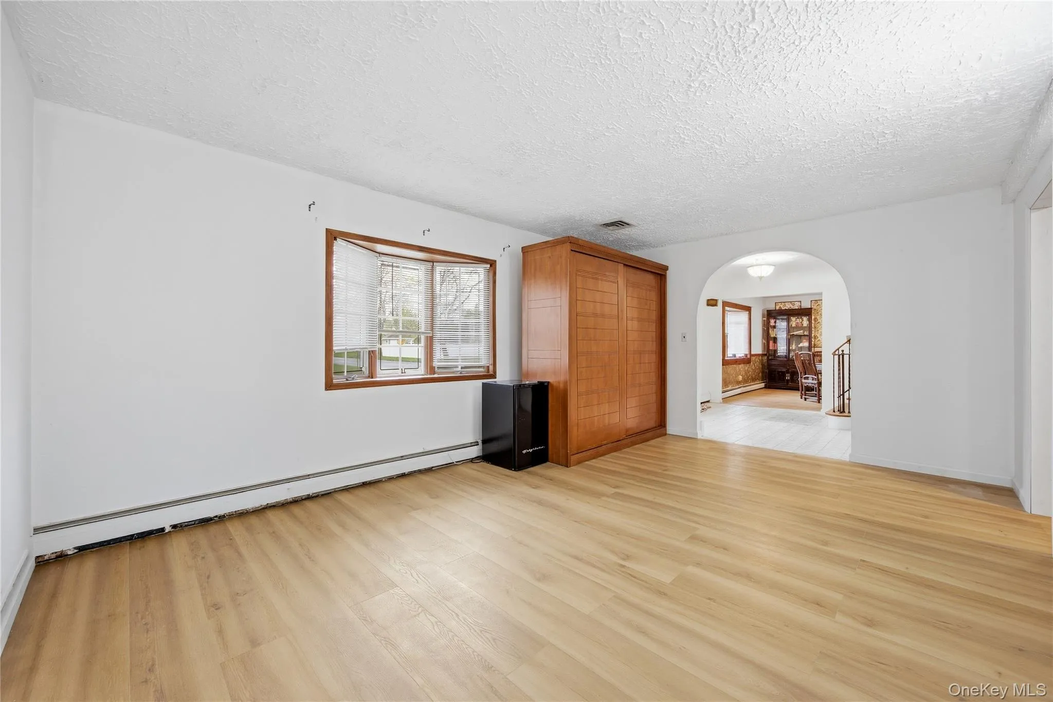 Open interior space featuring light wood-finish flooring, white walls, and a textured ceiling Open interior space featuring light wood-finish flooring, white walls, and a textured ceiling