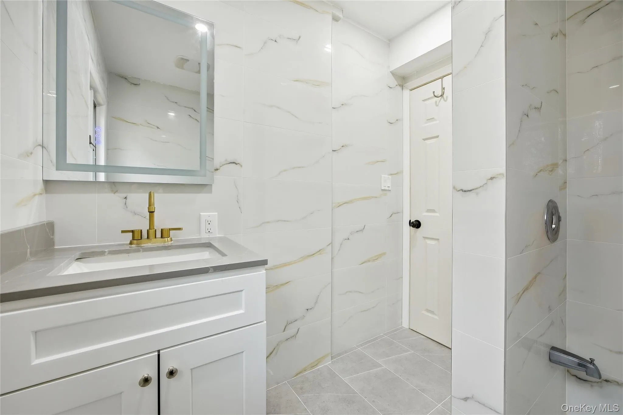 Bathroom featuring a white vanity with recessed panel cabinet doors, a gray countertop, an integrated rectangular sink, and a gold-finish faucet Bathroom featuring a white vanity with recessed panel cabinet doors, a gray countertop, an integrated rectangular sink, and a gold-finish faucet