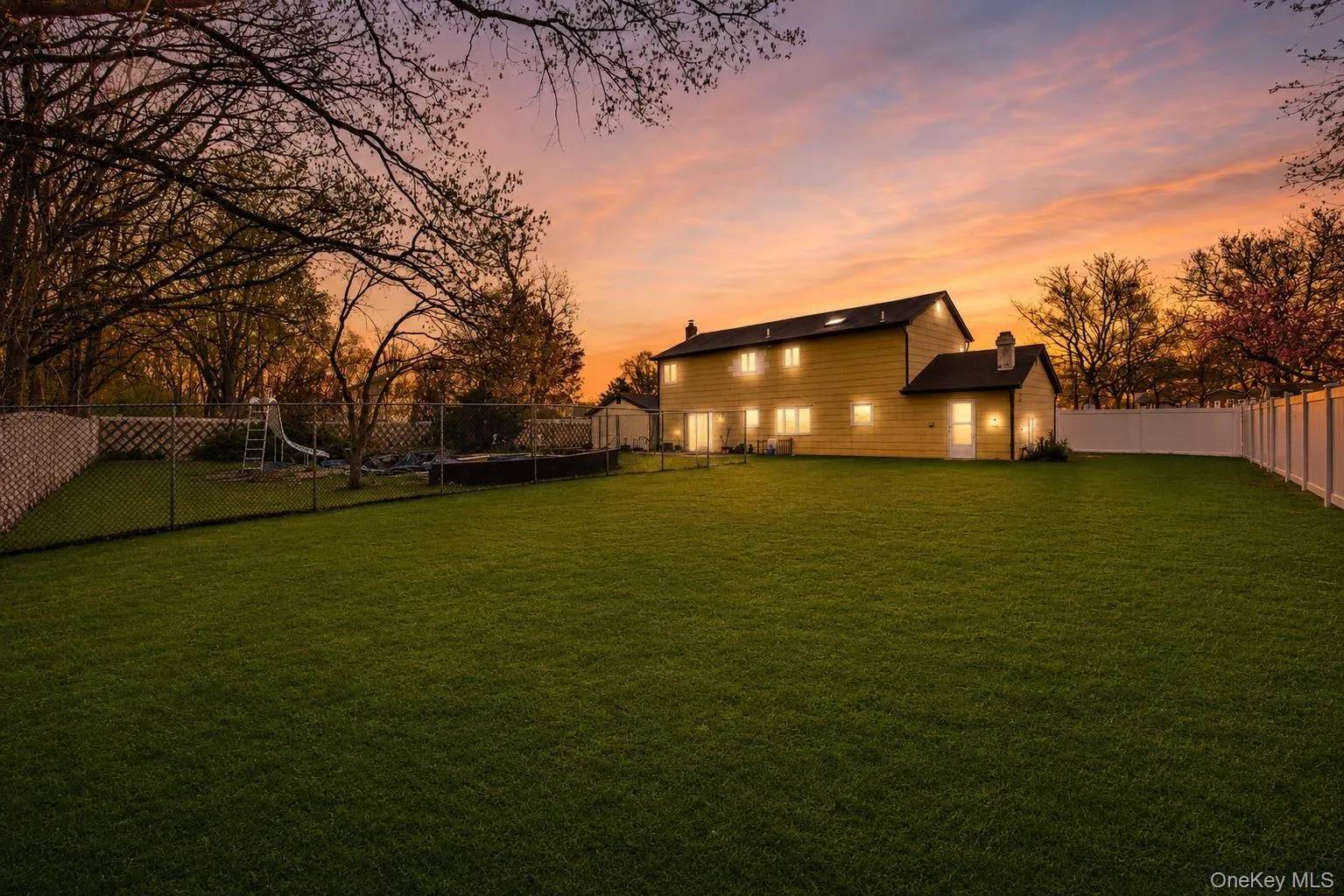 Expansive rear yard featuring a manicured lawn, established perimeter trees, and a white privacy fence Expansive rear yard featuring a manicured lawn, established perimeter trees, and a white privacy fence