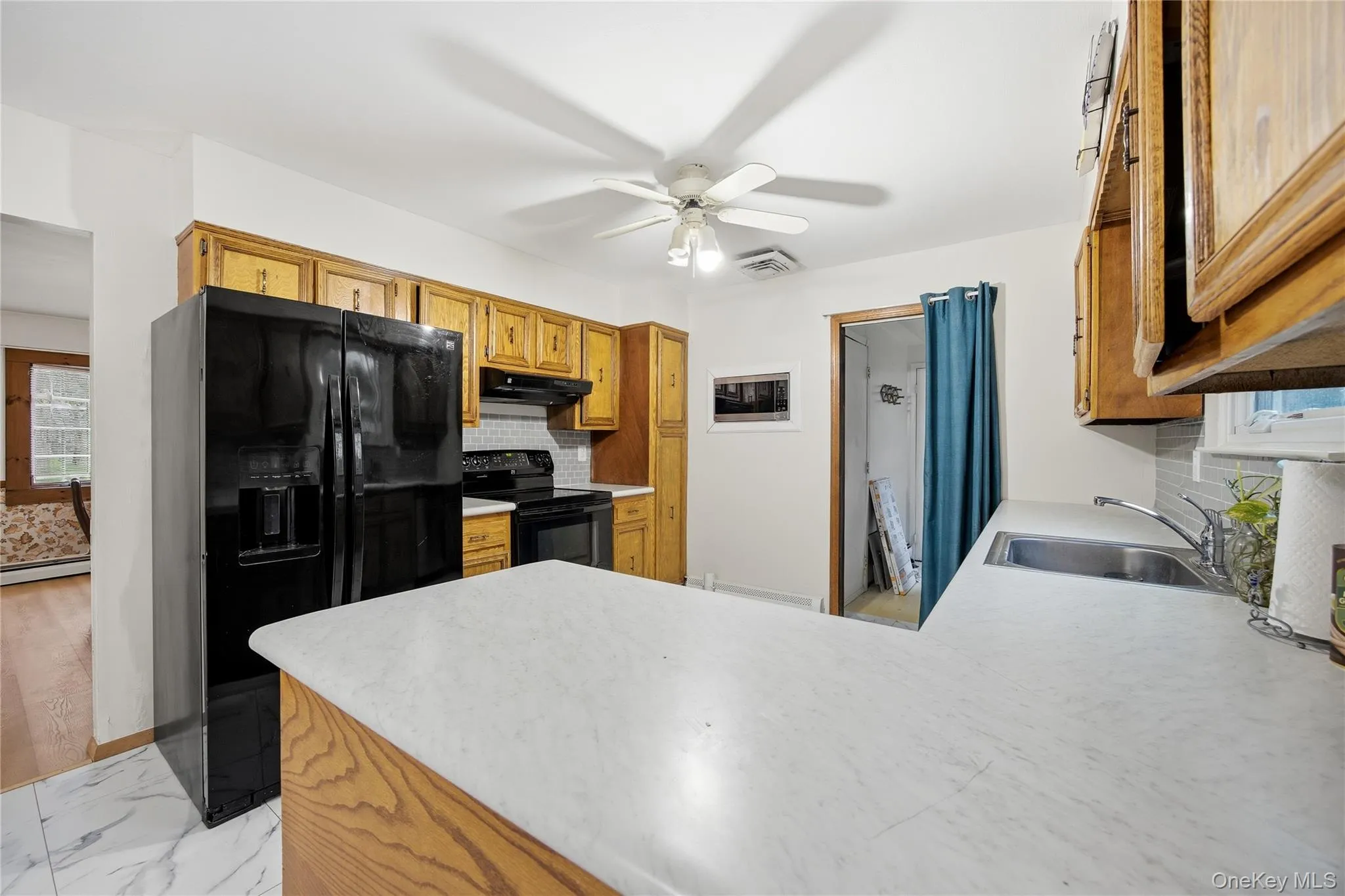 Kitchen featuring light wood cabinetry, white countertops, black appliance suite, and a stainless steel sink Kitchen featuring light wood cabinetry, white countertops, black appliance suite, and a stainless steel sink