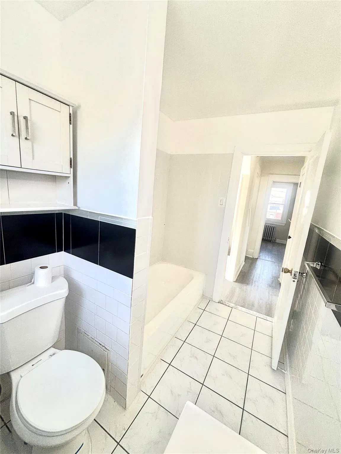 Bathroom featuring white square tile flooring with dark grout, a white toilet, and a built-in bathtub. Bathroom featuring white square tile flooring with dark grout, a white toilet, and a built-in bathtub.