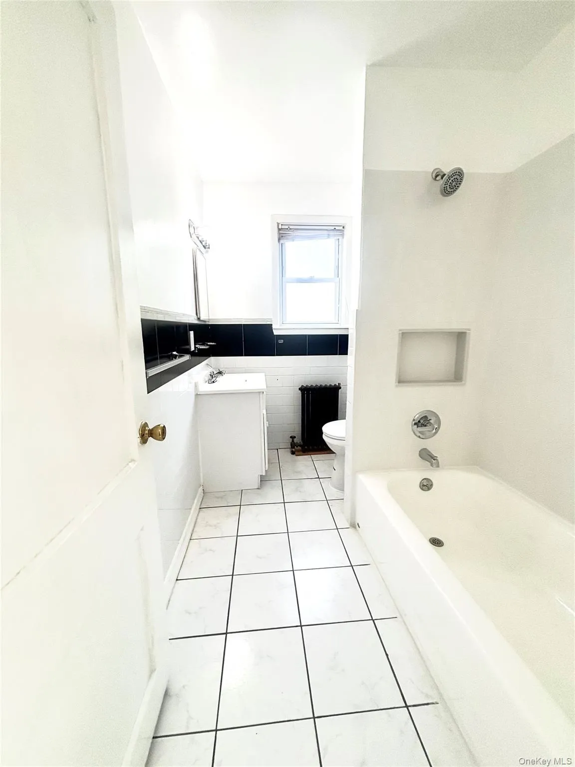 Bathroom featuring a white bathtub with chrome fixtures, a built-in shower niche, and white tiled flooring. Bathroom featuring a white bathtub with chrome fixtures, a built-in shower niche, and white tiled flooring.