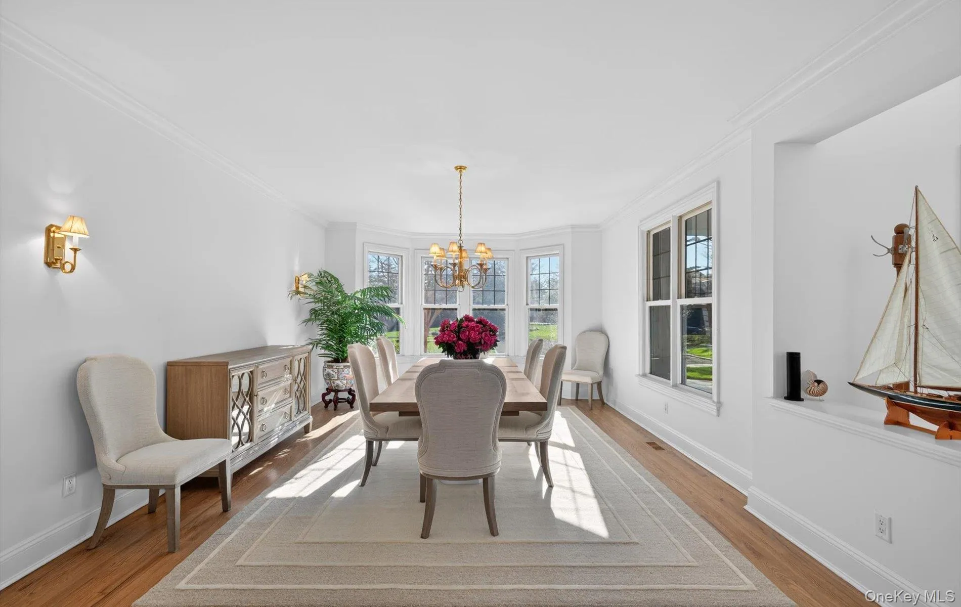 Formal dining area featuring hardwood flooring, crown molding, a bay window, and a built-in wall niche Formal dining area featuring hardwood flooring, crown molding, a bay window, and a built-in wall niche