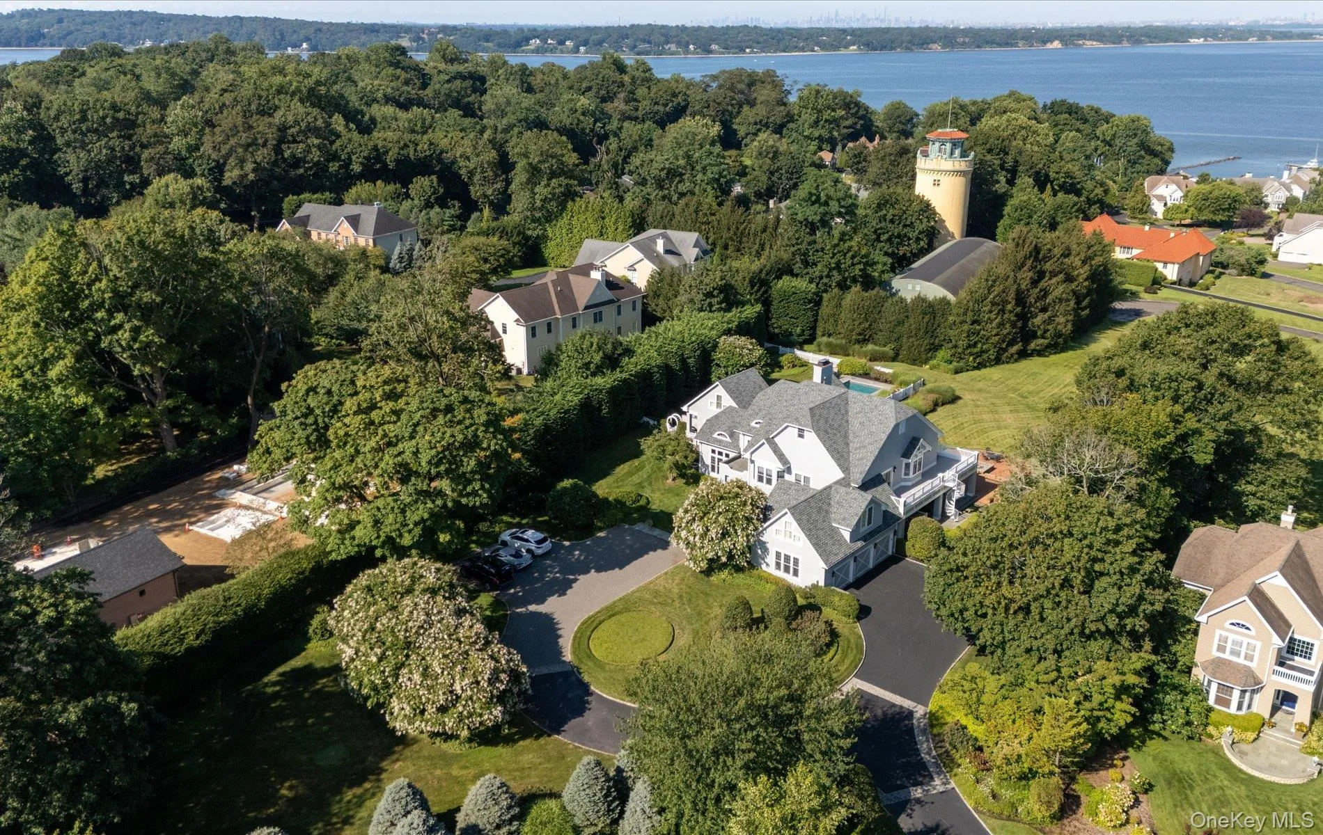 Expansive property featuring a multi-level residence with a gray shingle roof, a circular asphalt driveway, and mature landscaping Expansive property featuring a multi-level residence with a gray shingle roof, a circular asphalt driveway, and mature landscaping