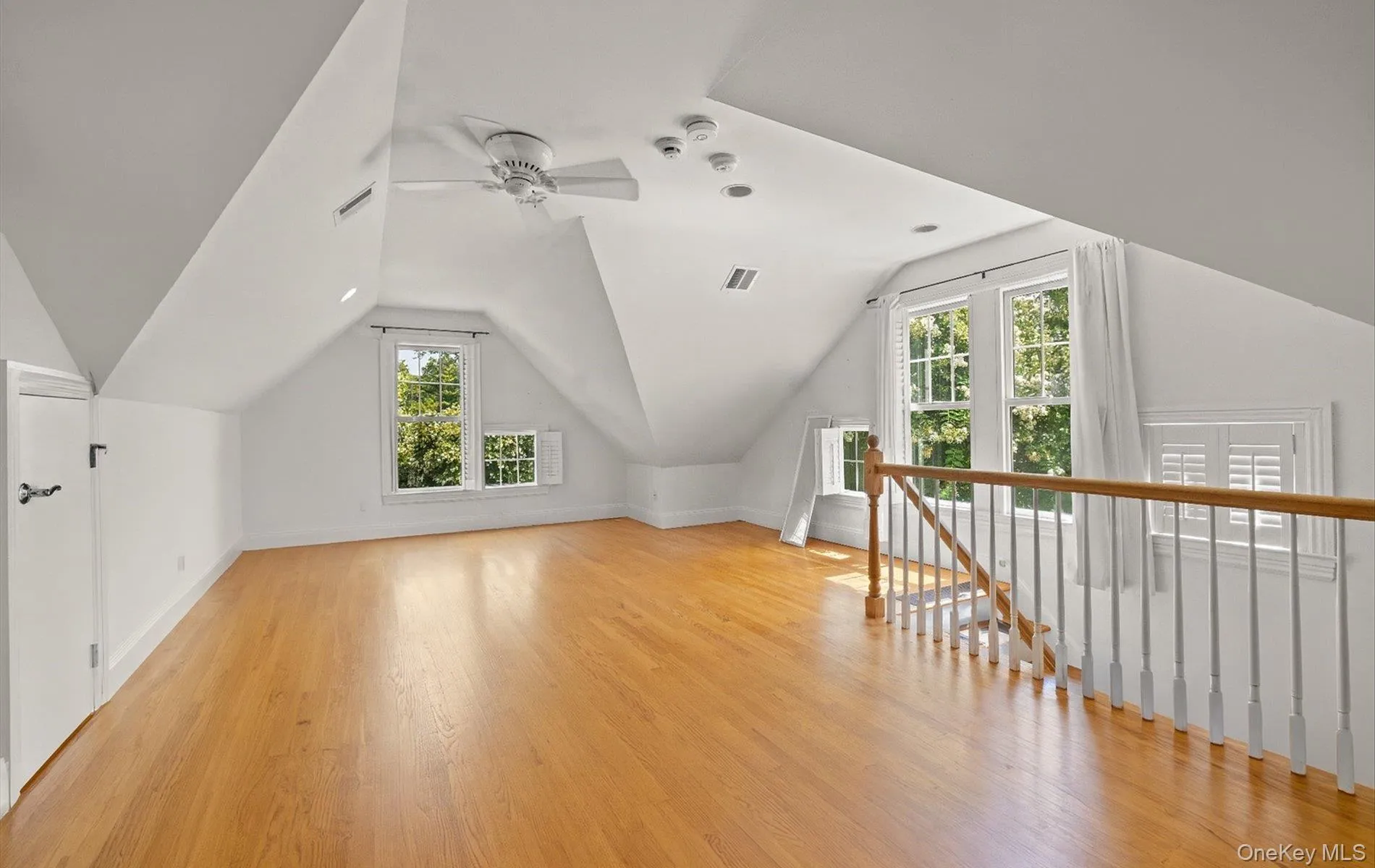 Spacious attic room featuring wood-finish flooring, vaulted ceilings, and multiple windows with exterior views Spacious attic room featuring wood-finish flooring, vaulted ceilings, and multiple windows with exterior views