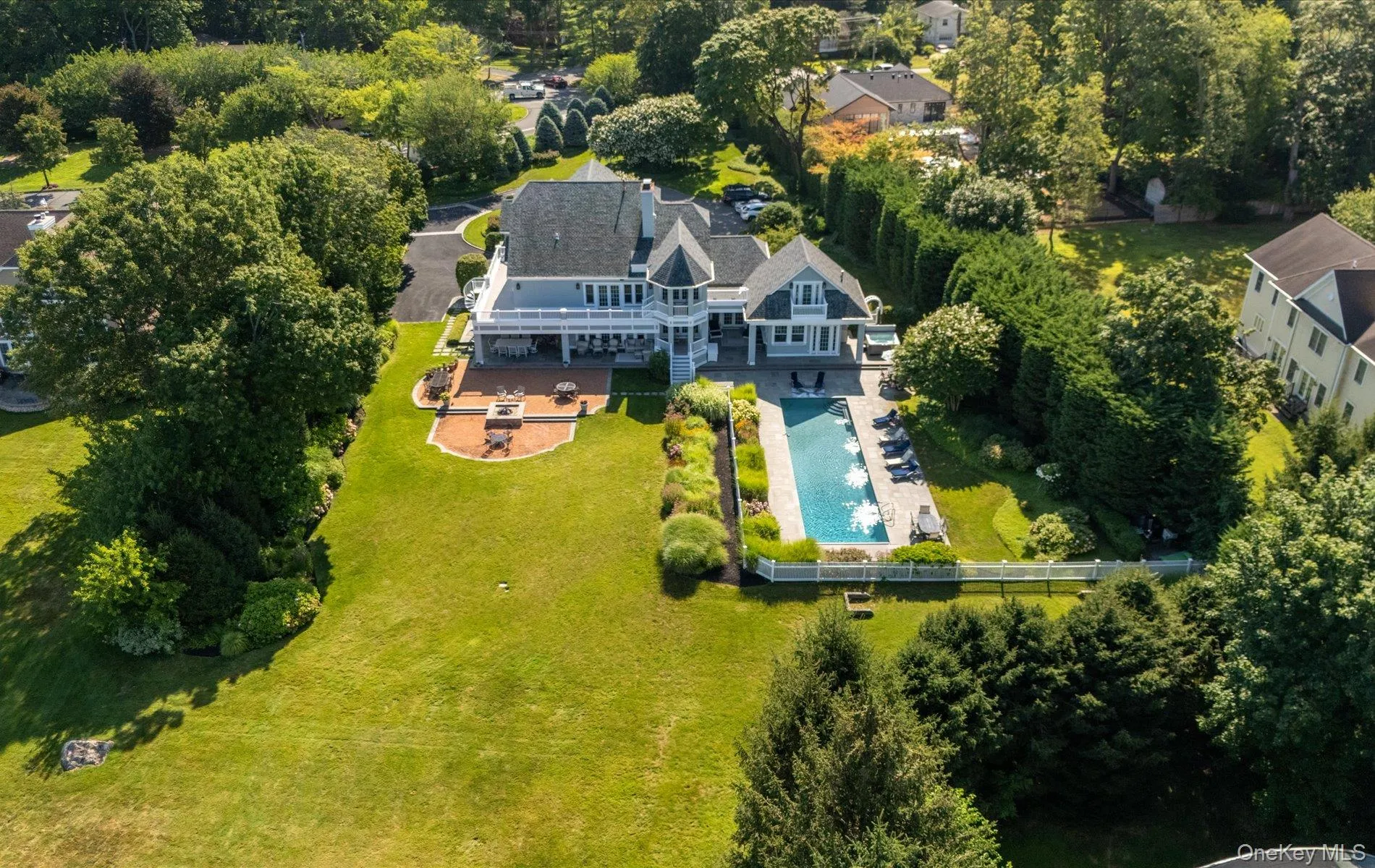Expansive backyard featuring a rectangular swimming pool, a brick paver patio with a built-in fire pit, and extensive landscaping with mature trees and shrubs Expansive backyard featuring a rectangular swimming pool, a brick paver patio with a built-in fire pit, and extensive landscaping with mature trees and shrubs