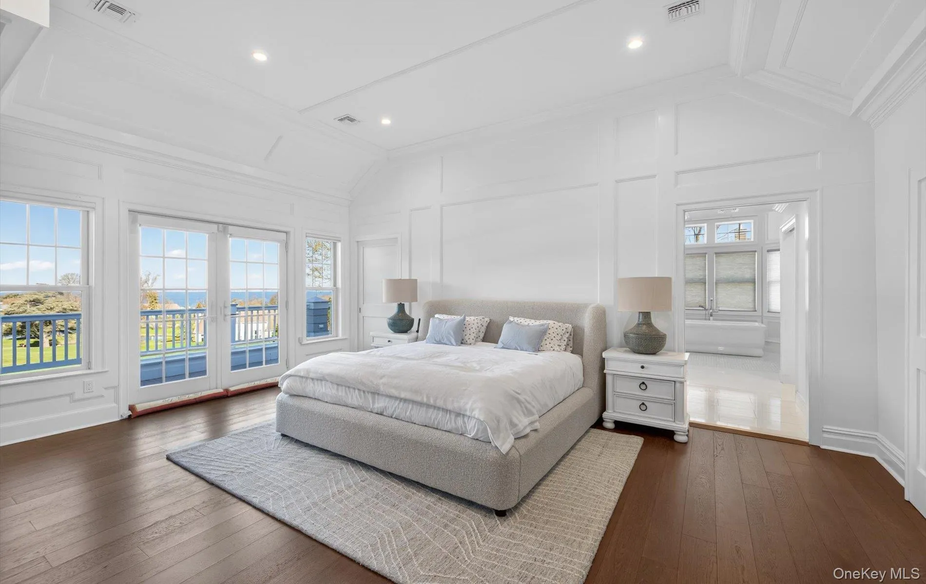 Spacious bedroom featuring dark wood-finish flooring, white paneling, and an ornate tray ceiling Spacious bedroom featuring dark wood-finish flooring, white paneling, and an ornate tray ceiling