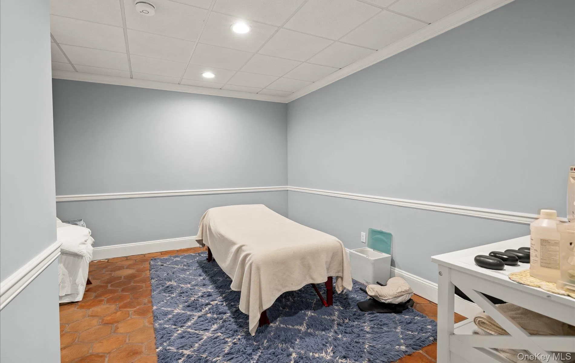 Room featuring hexagonal terracotta-style flooring, light-toned walls with chair rail molding, and a drop ceiling with recessed lighting Room featuring hexagonal terracotta-style flooring, light-toned walls with chair rail molding, and a drop ceiling with recessed lighting