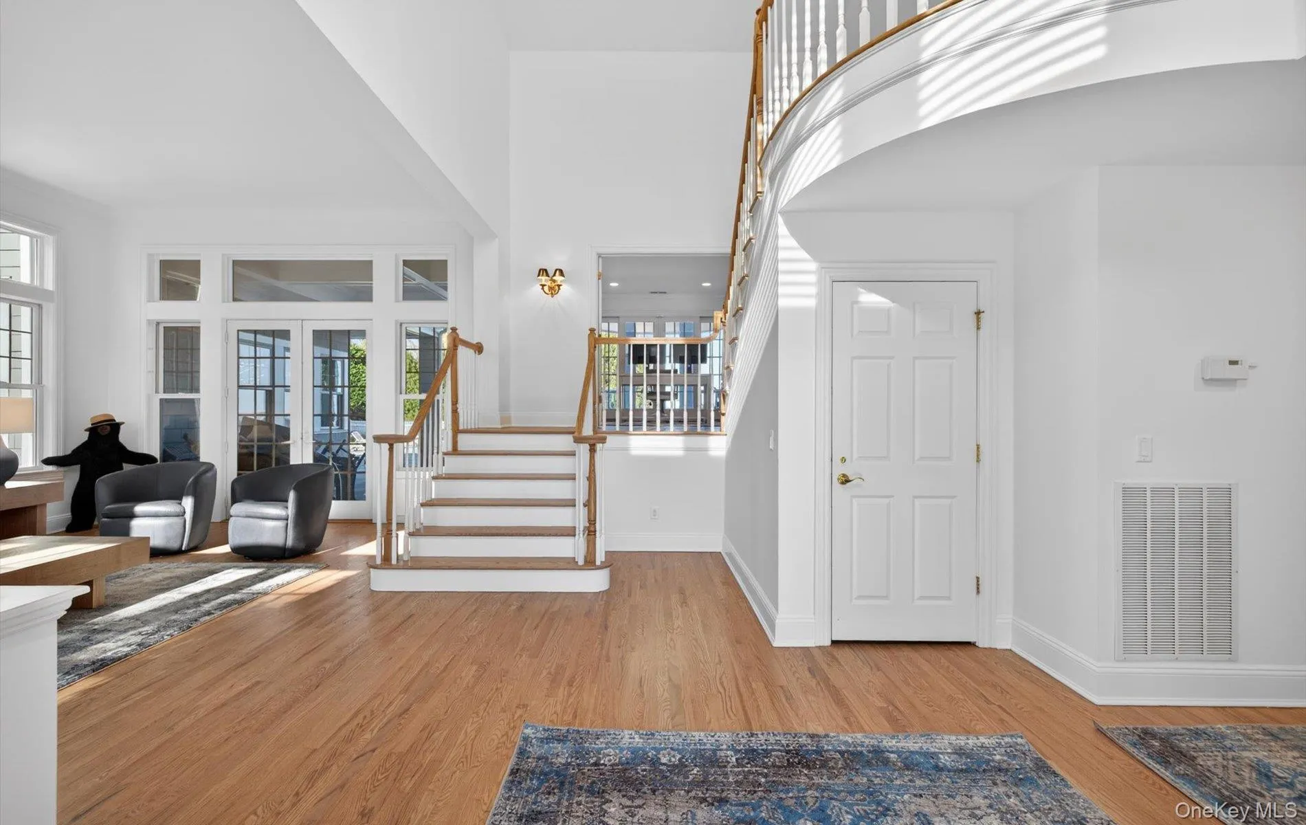 Two-story entry foyer featuring wood-finish flooring, a grand staircase with wood newel posts and handrails, and a second-story curved landing Two-story entry foyer featuring wood-finish flooring, a grand staircase with wood newel posts and handrails, and a second-story curved landing
