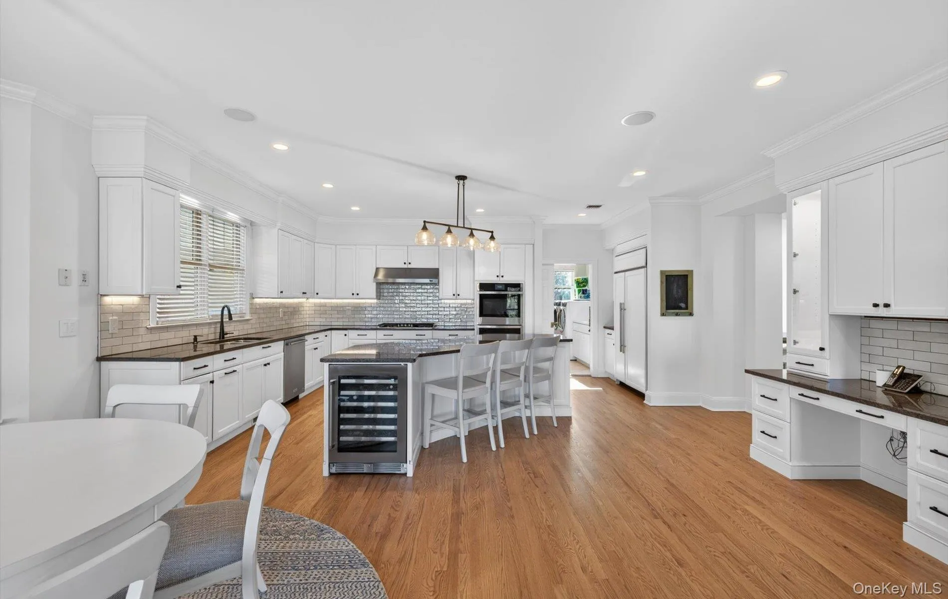 Gourmet kitchen featuring a central island with integrated beverage refrigerator, white cabinetry, dark countertops, and wood-finish flooring Gourmet kitchen featuring a central island with integrated beverage refrigerator, white cabinetry, dark countertops, and wood-finish flooring