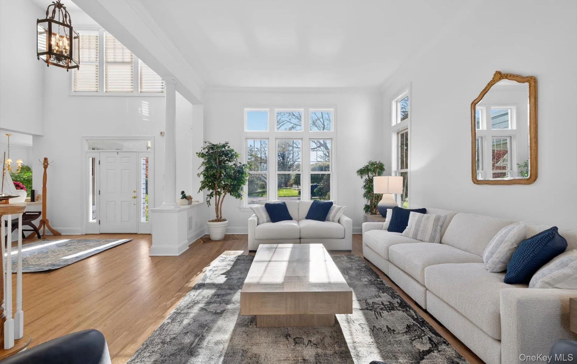 Spacious living area featuring high ceilings, hardwood flooring, large windows, a prominent entry door with sidelights, and a decorative chandelier Spacious living area featuring high ceilings, hardwood flooring, large windows, a prominent entry door with sidelights, and a decorative chandelier