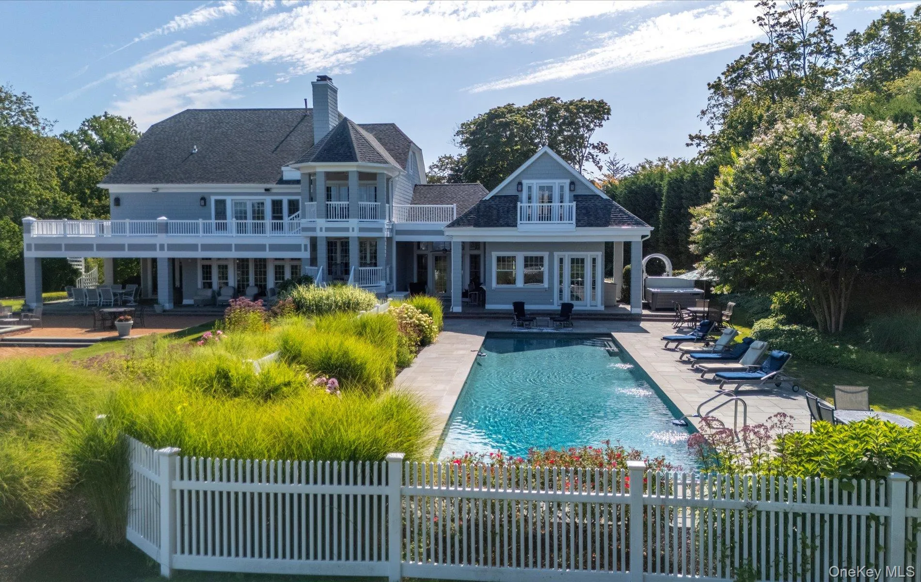 Expansive outdoor living area featuring a rectangular in-ground pool with surrounding patio, a separate hot tub, and a two-story residence with multiple balconies and a covered patio Expansive outdoor living area featuring a rectangular in-ground pool with surrounding patio, a separate hot tub, and a two-story residence with multiple balconies and a covered patio
