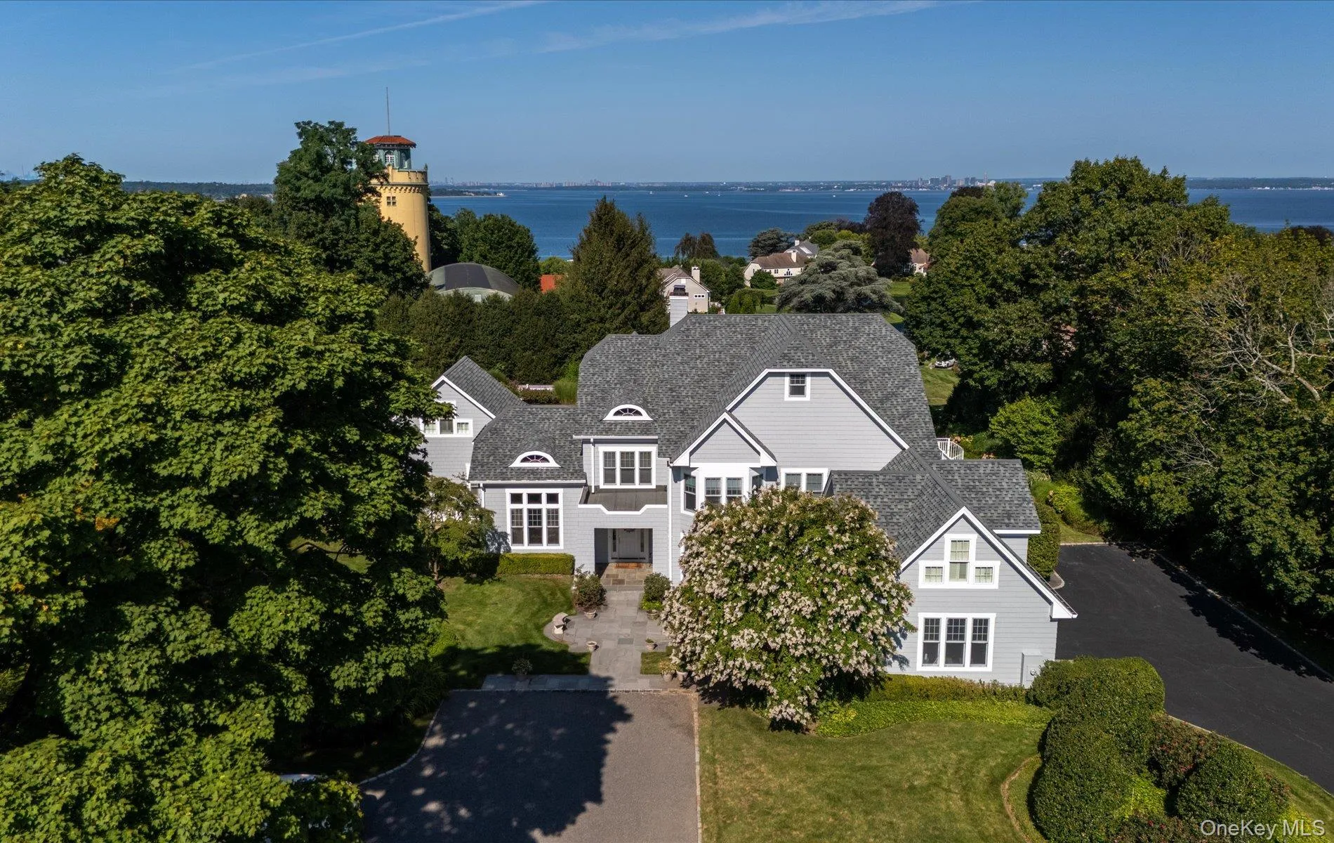 Gray shingle-style residence featuring a multi-gabled roofline, dormer windows, and a paved driveway Gray shingle-style residence featuring a multi-gabled roofline, dormer windows, and a paved driveway