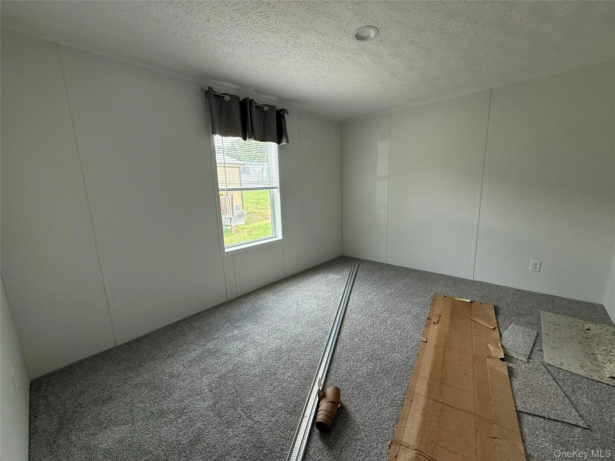 Empty room with a textured ceiling, a decorative wall, and carpet flooring Empty room with a textured ceiling, a decorative wall, and carpet flooring