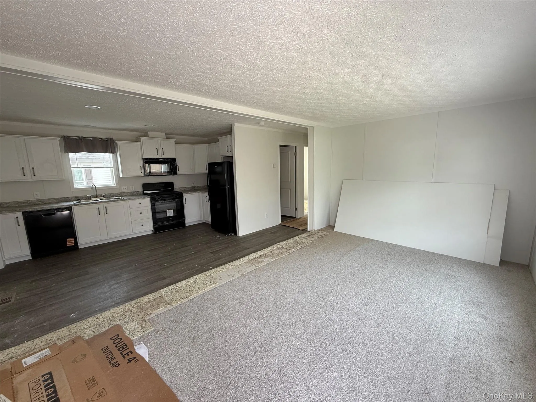 Unfurnished living room with a textured ceiling, dark wood-type flooring, and dark carpet Unfurnished living room with a textured ceiling, dark wood-type flooring, and dark carpet