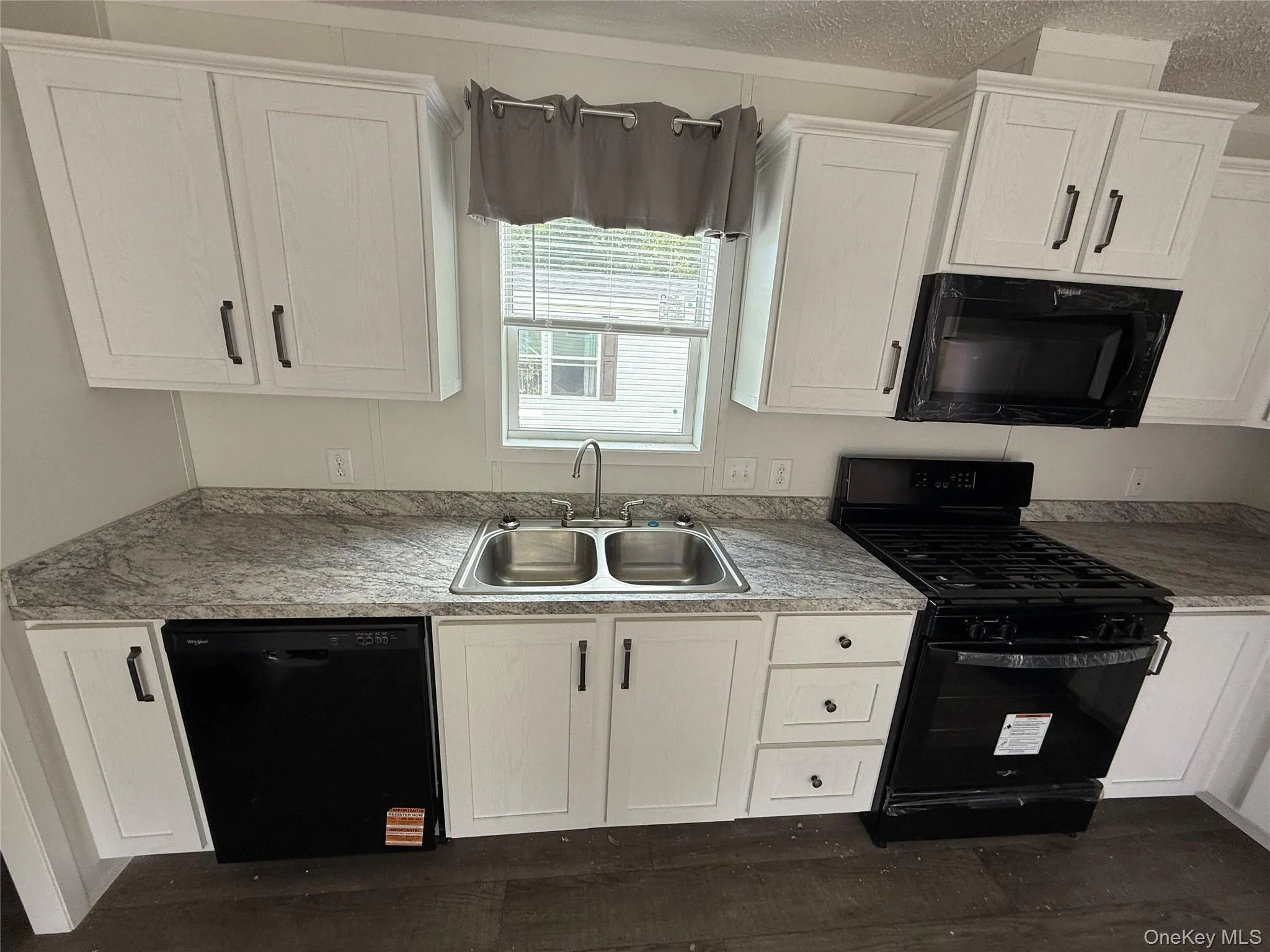 Kitchen featuring black appliances, white cabinetry, light countertops, and a textured ceiling Kitchen featuring black appliances, white cabinetry, light countertops, and a textured ceiling