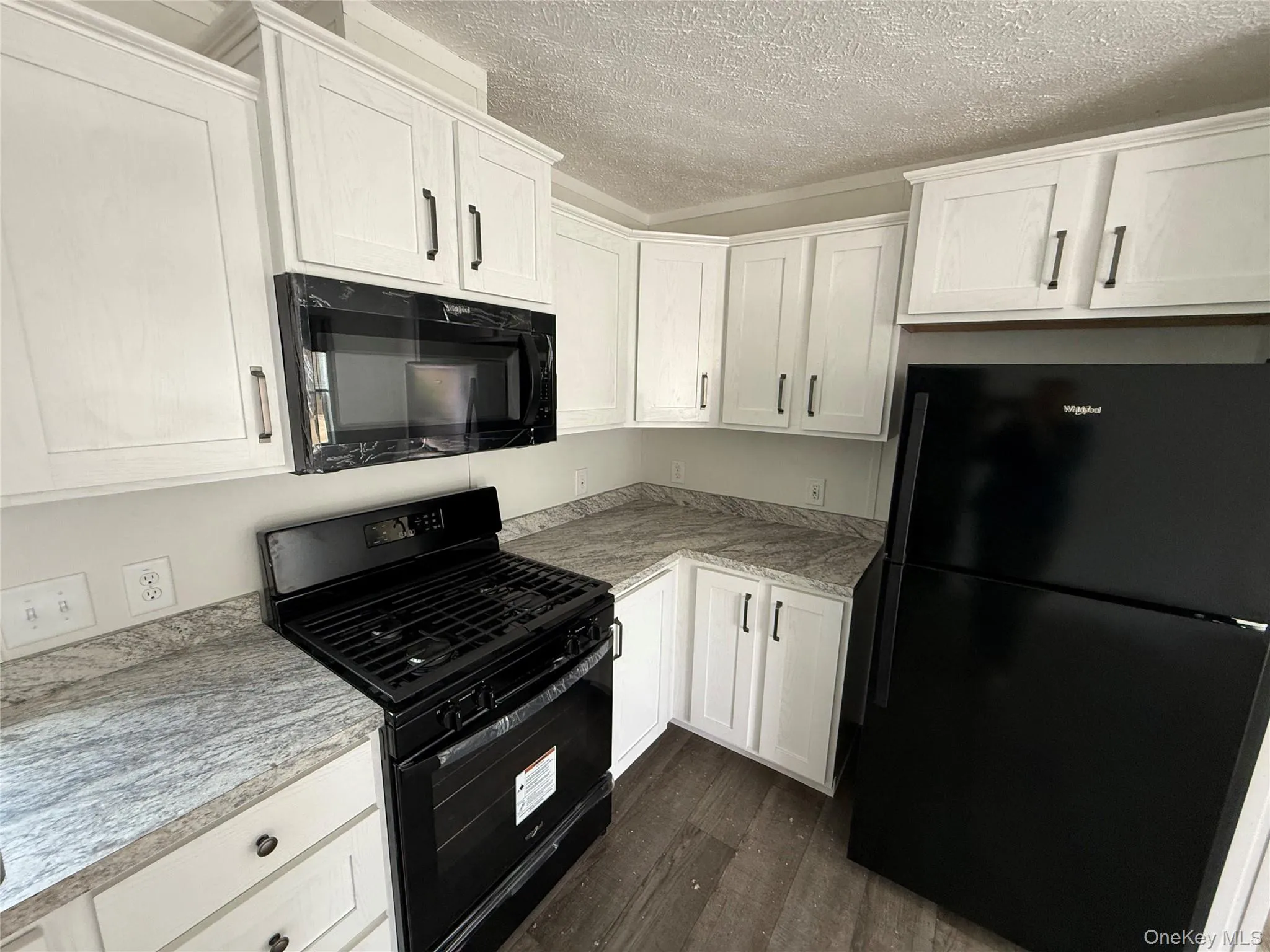 Kitchen with black appliances, dark wood-style flooring, white cabinetry, a textured ceiling, and light stone countertops Kitchen with black appliances, dark wood-style flooring, white cabinetry, a textured ceiling, and light stone countertops