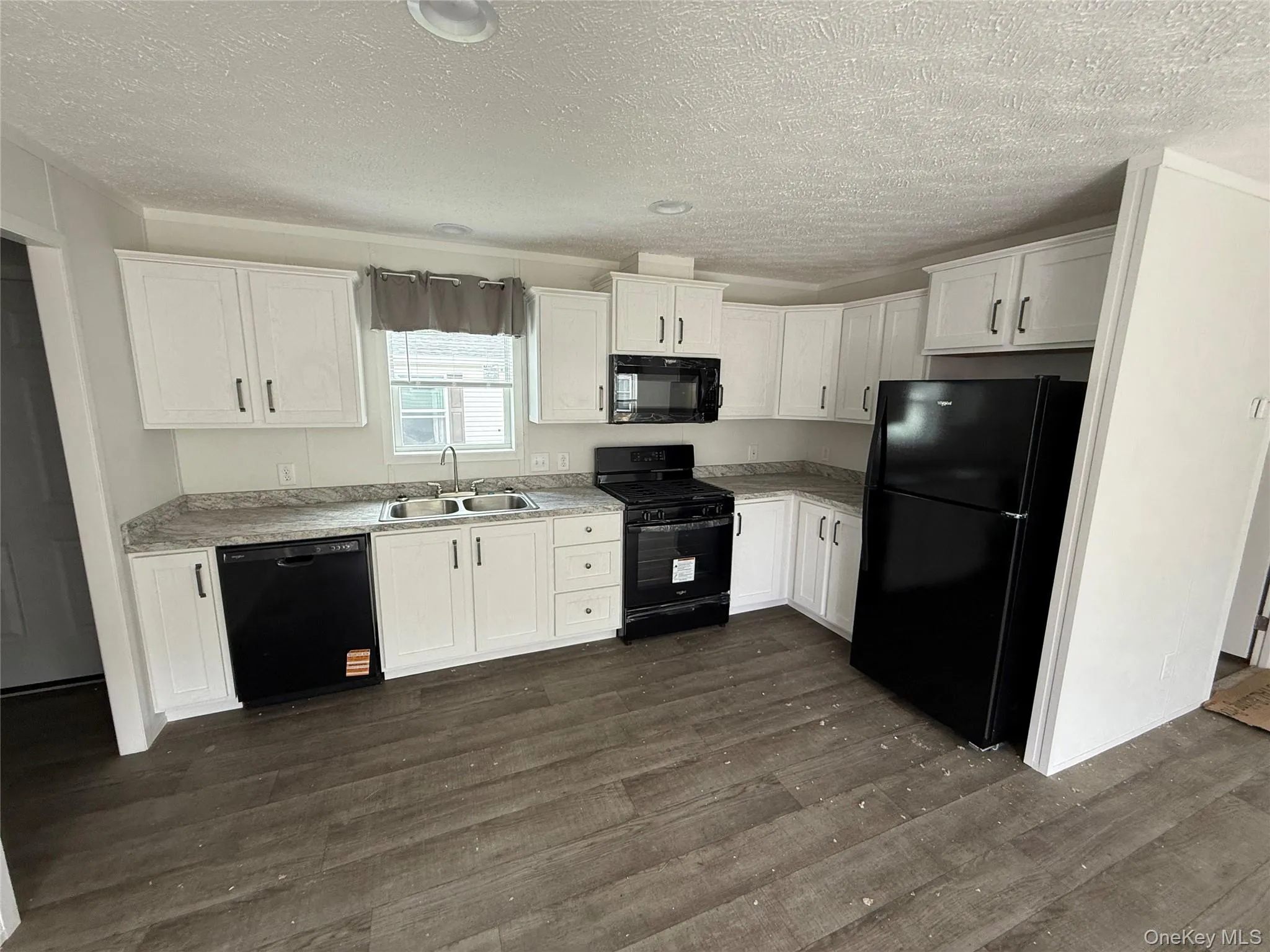 Kitchen featuring black appliances, white cabinets, dark wood-style flooring, light countertops, and a textured ceiling Kitchen featuring black appliances, white cabinets, dark wood-style flooring, light countertops, and a textured ceiling