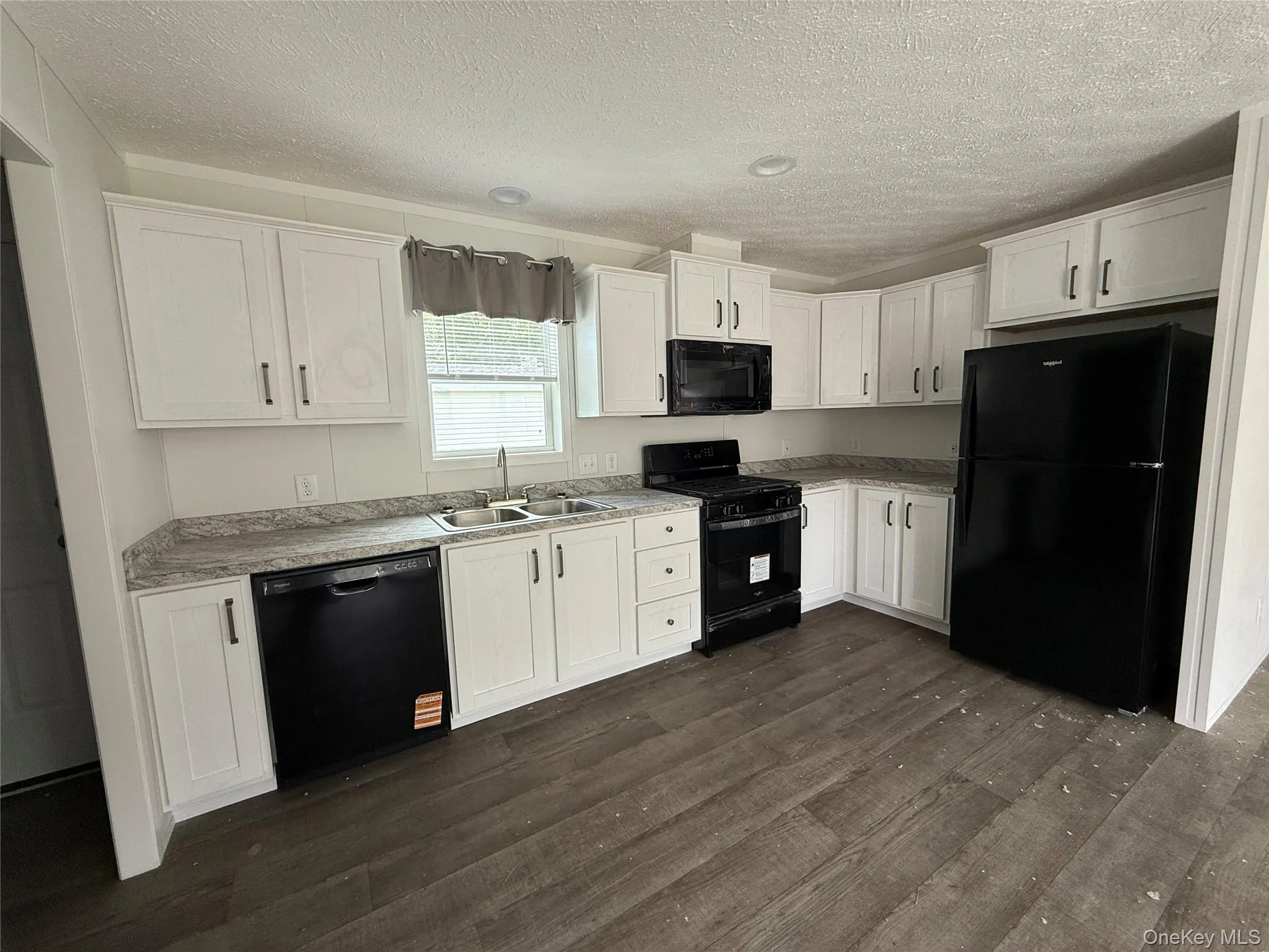 Kitchen with black appliances, white cabinetry, dark wood-style flooring, light countertops, and a textured ceiling Kitchen with black appliances, white cabinetry, dark wood-style flooring, light countertops, and a textured ceiling
