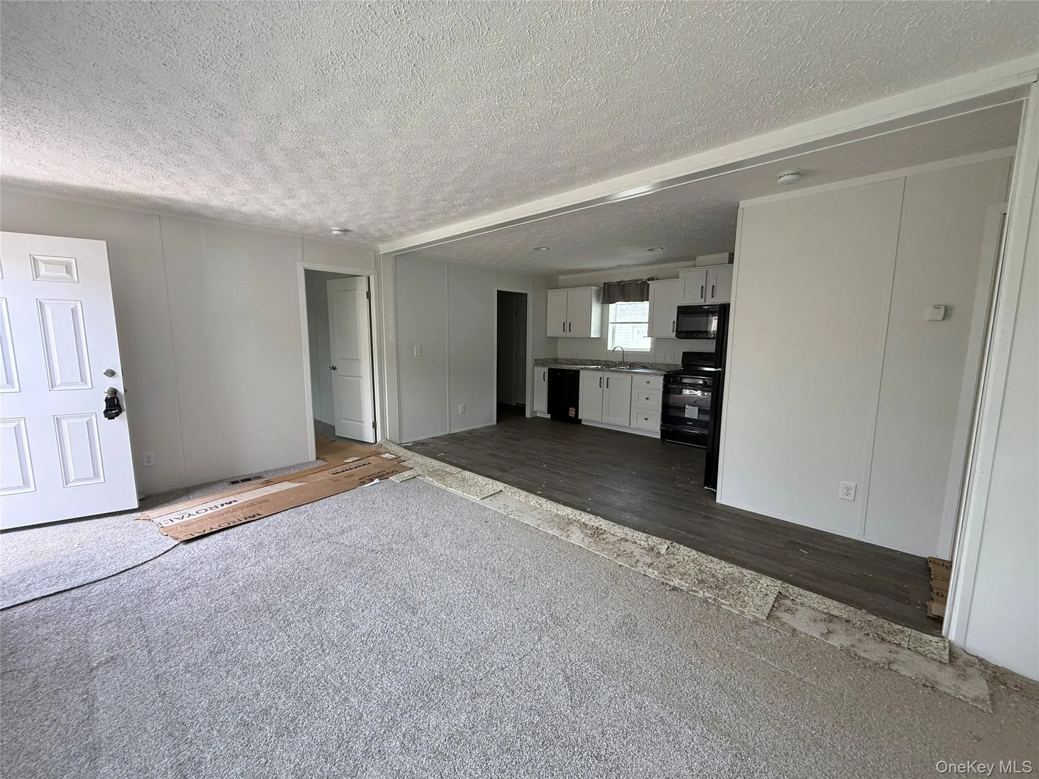 Unfurnished living room featuring a textured ceiling, dark wood-style flooring, and dark carpet Unfurnished living room featuring a textured ceiling, dark wood-style flooring, and dark carpet