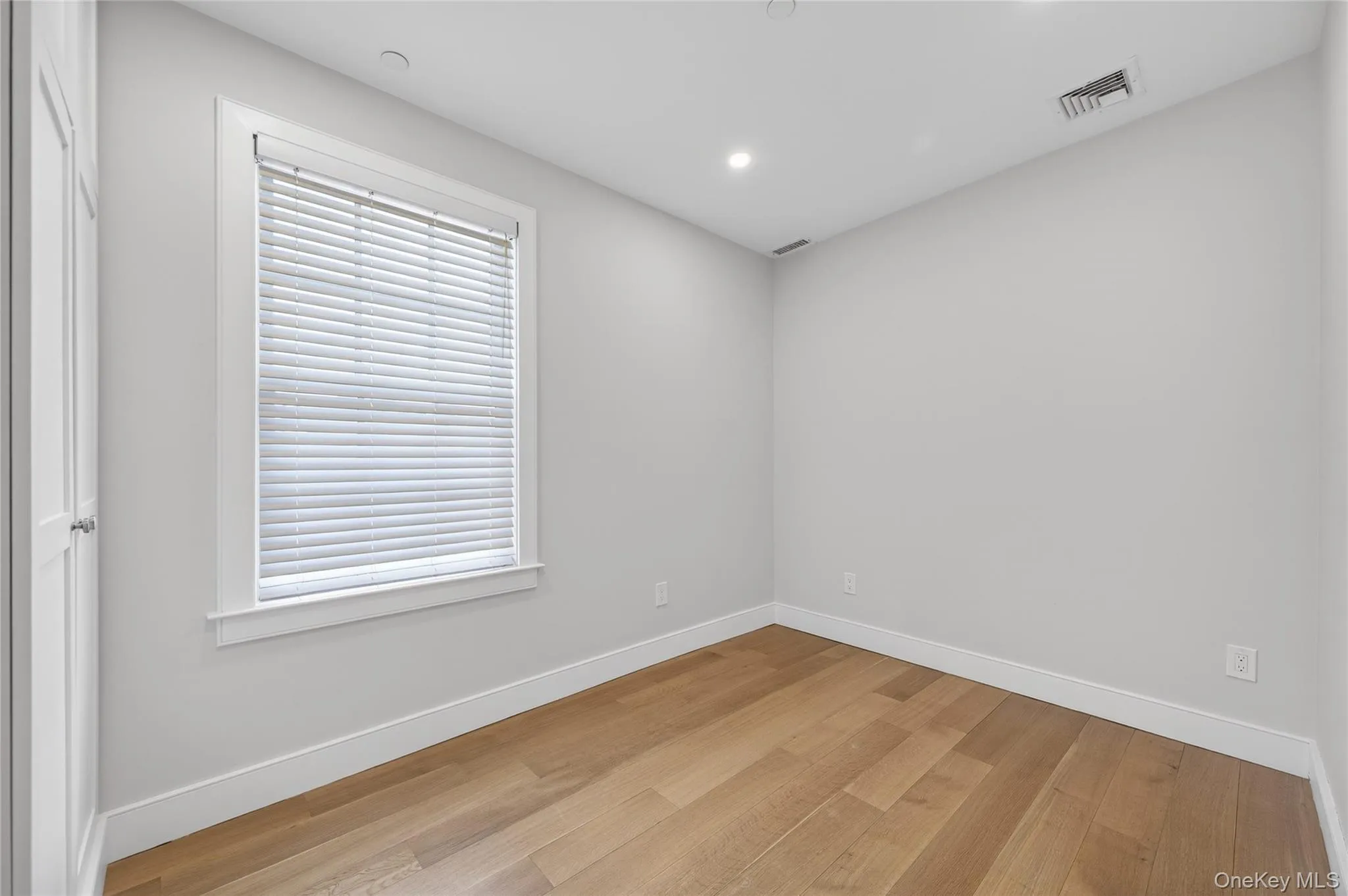Room featuring wood-finish flooring, white baseboards, a white-framed window with blinds, and recessed lighting Room featuring wood-finish flooring, white baseboards, a white-framed window with blinds, and recessed lighting