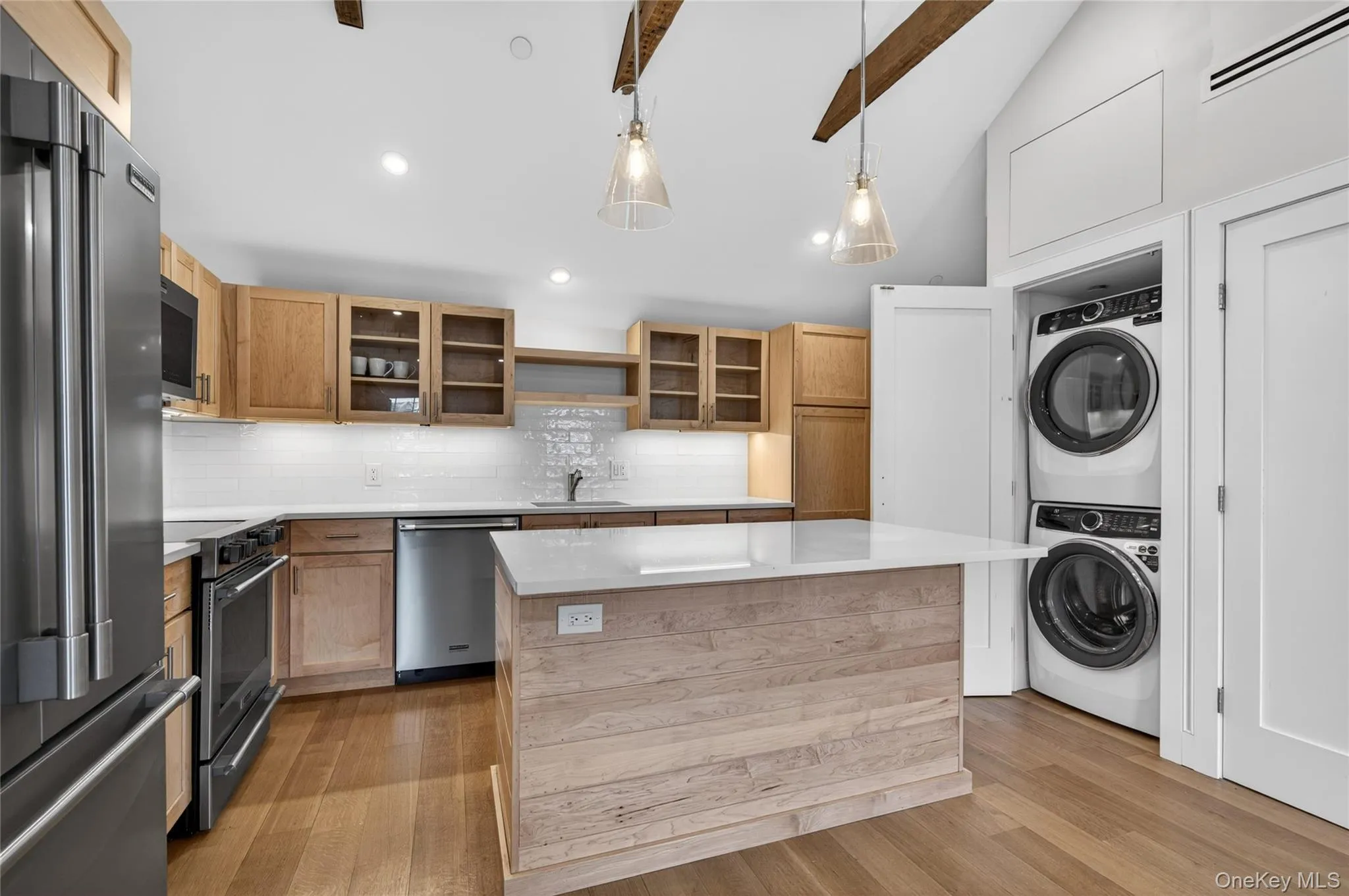 Modern kitchen featuring a central island with a light wood finish, white quartz countertop, and integrated outlets and washer dryer Modern kitchen featuring a central island with a light wood finish, white quartz countertop, and integrated outlets and washer dryer