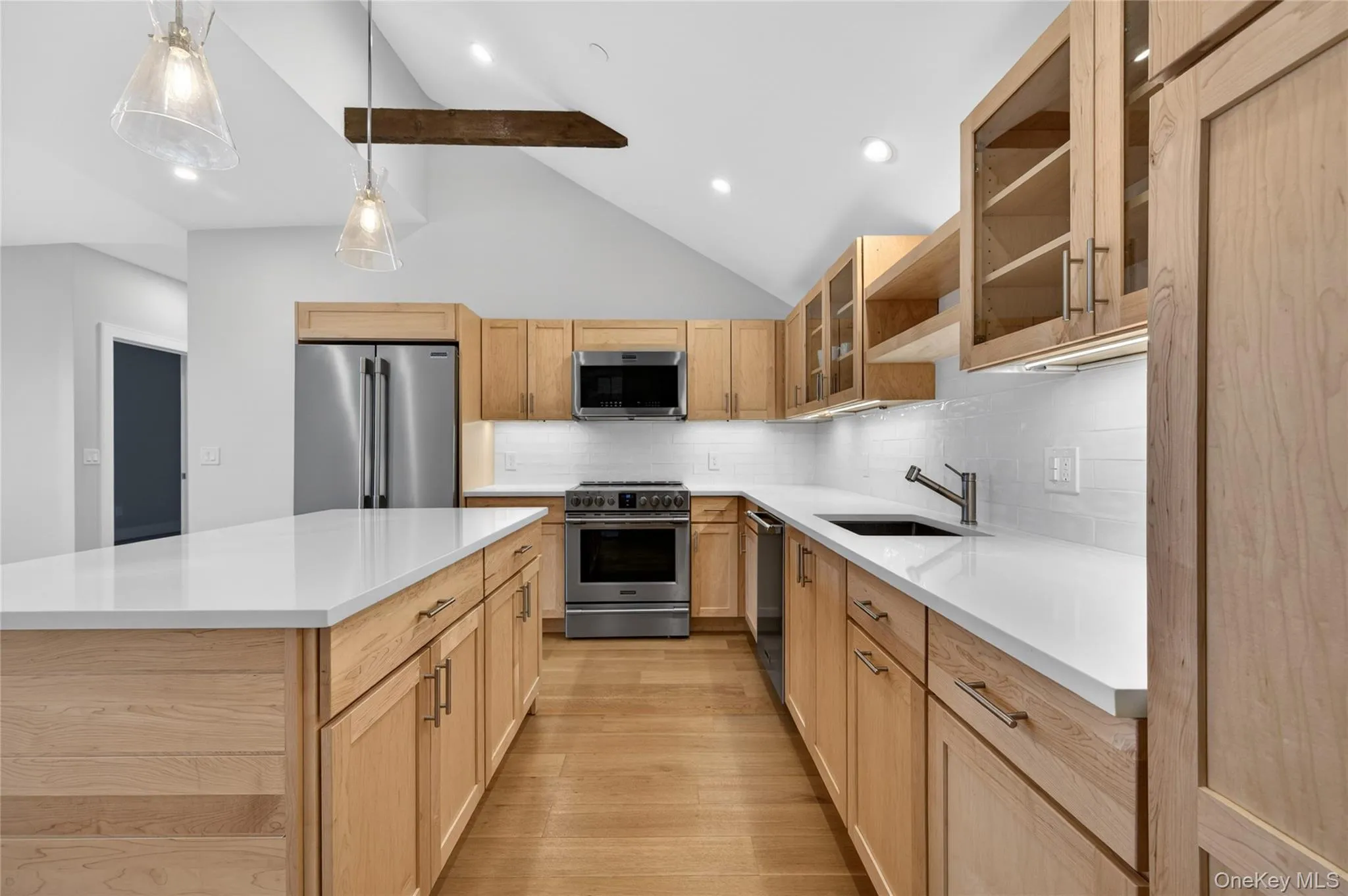 Gourmet kitchen featuring a spacious island with white countertops, light wood cabinetry, stainless steel appliances, and vaulted ceilings with exposed beam Gourmet kitchen featuring a spacious island with white countertops, light wood cabinetry, stainless steel appliances, and vaulted ceilings with exposed beam