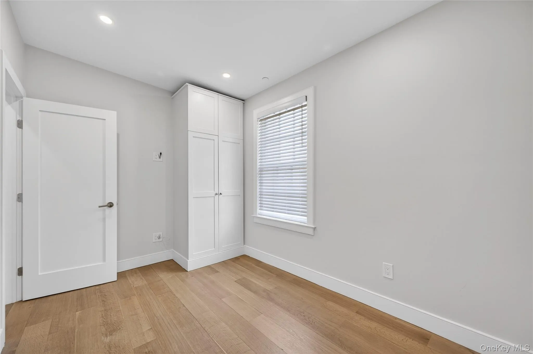Room featuring wood-finish flooring, recessed lighting, and a window with blinds Room featuring wood-finish flooring, recessed lighting, and a window with blinds