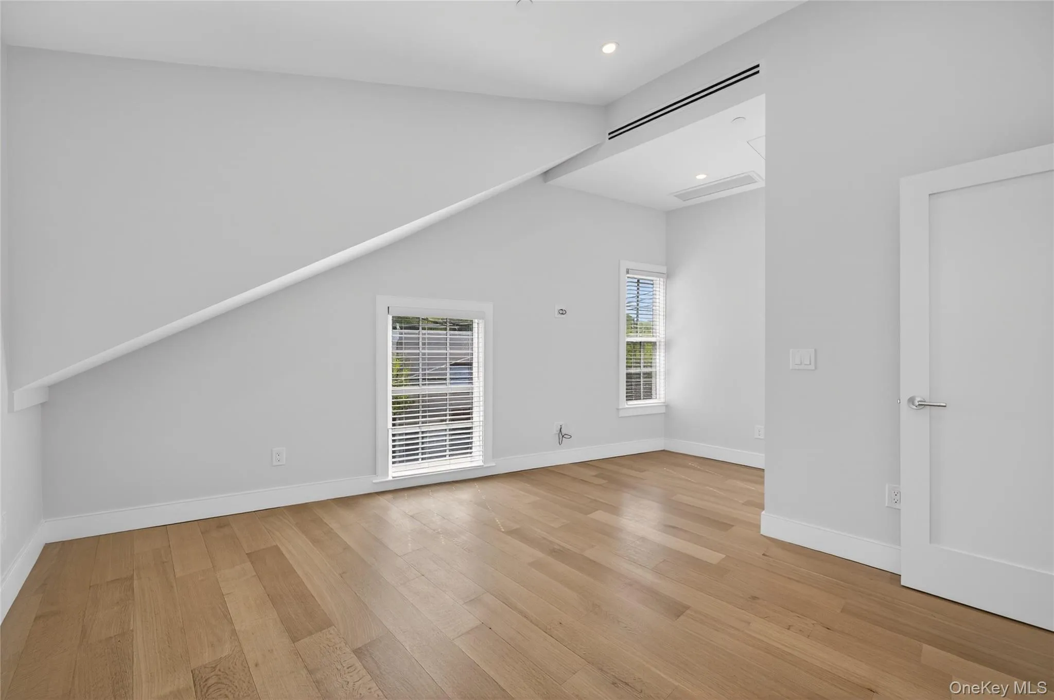 Spacious room featuring wood-finish flooring, recessed lighting, and a sloped ceiling with architectural detail Spacious room featuring wood-finish flooring, recessed lighting, and a sloped ceiling with architectural detail