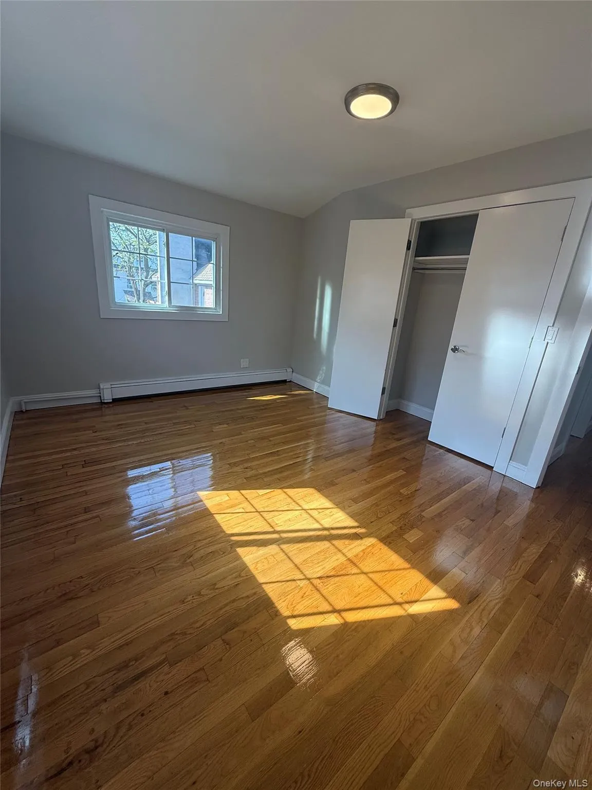 Hardwood flooring throughout featuring a window with white trim, a flush mount ceiling light, and a bi-fold door closet with a hanging rod Hardwood flooring throughout featuring a window with white trim, a flush mount ceiling light, and a bi-fold door closet with a hanging rod