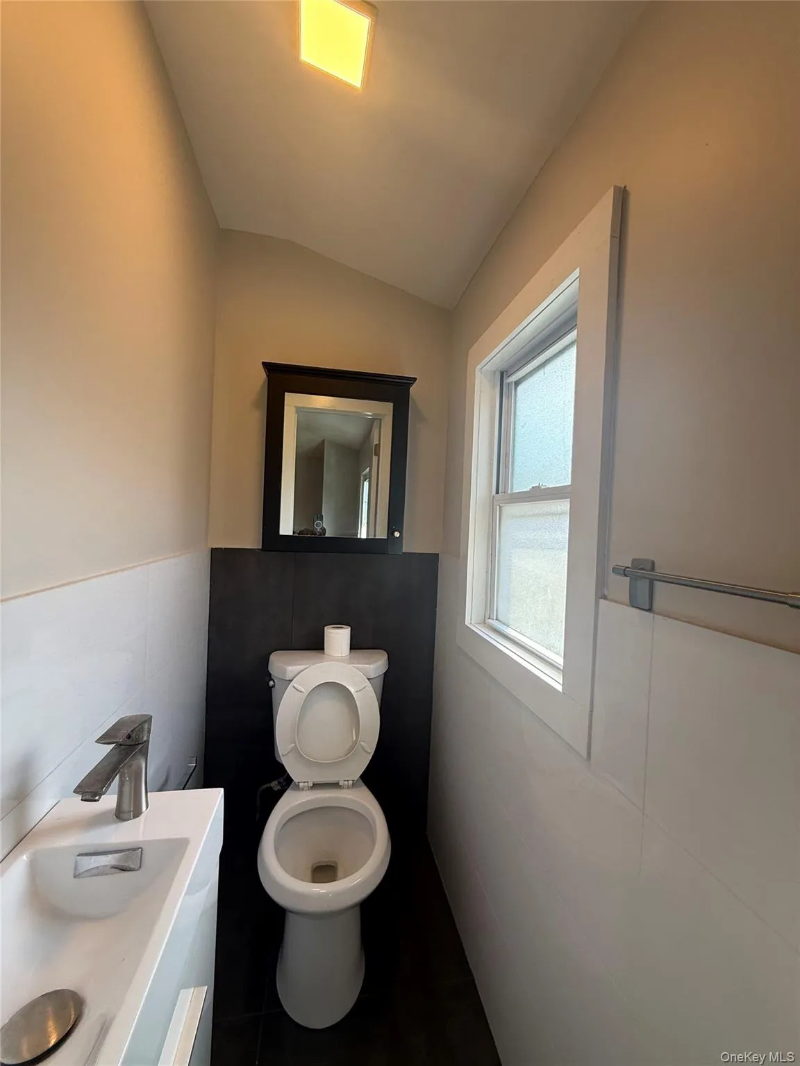 Compact bathroom featuring a wall-mounted vanity with integrated sink, chrome faucet, and a wall-mounted dark-framed mirror Compact bathroom featuring a wall-mounted vanity with integrated sink, chrome faucet, and a wall-mounted dark-framed mirror