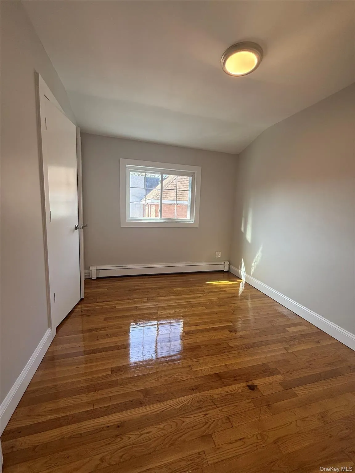 Hardwood flooring with natural finish, white baseboards, and a single window with white trim Hardwood flooring with natural finish, white baseboards, and a single window with white trim