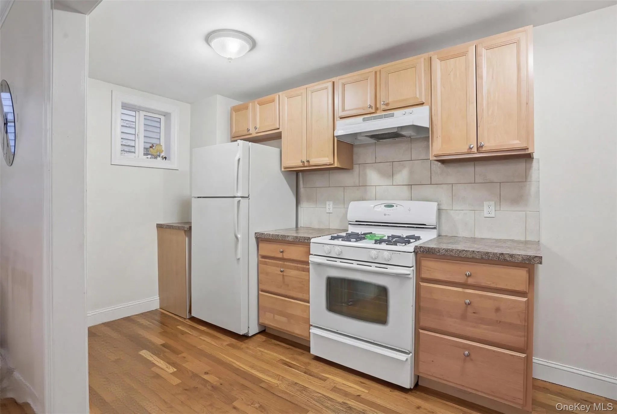 Kitchen featuring wood-finish flooring, light wood cabinetry, stone-look countertops, and a tile backsplash Kitchen featuring wood-finish flooring, light wood cabinetry, stone-look countertops, and a tile backsplash