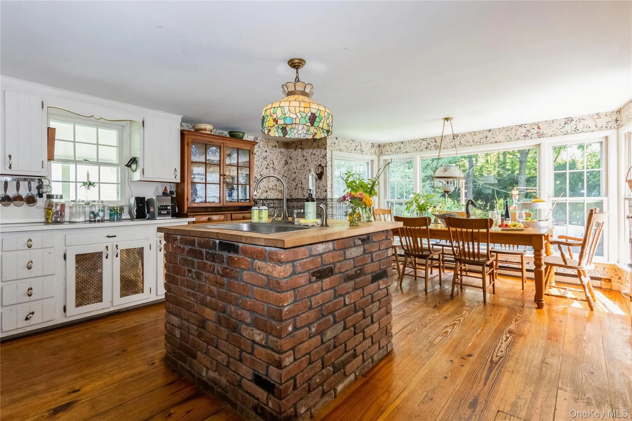Kitchen with white cabinetry, wood flooring, a center island with sink, pendant lighting, and wallpapered walls Kitchen with white cabinetry, wood flooring, a center island with sink, pendant lighting, and wallpapered walls
