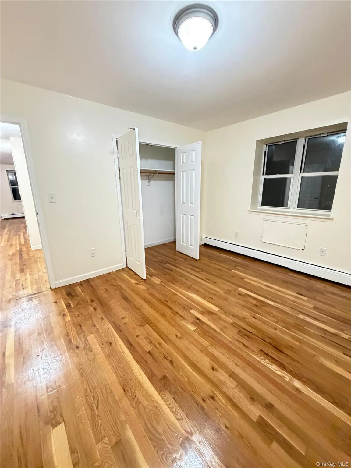 Room featuring wood-finish flooring, neutral wall paint, a built-in closet with bifold doors, and a ceiling-mounted light fixture Room featuring wood-finish flooring, neutral wall paint, a built-in closet with bifold doors, and a ceiling-mounted light fixture