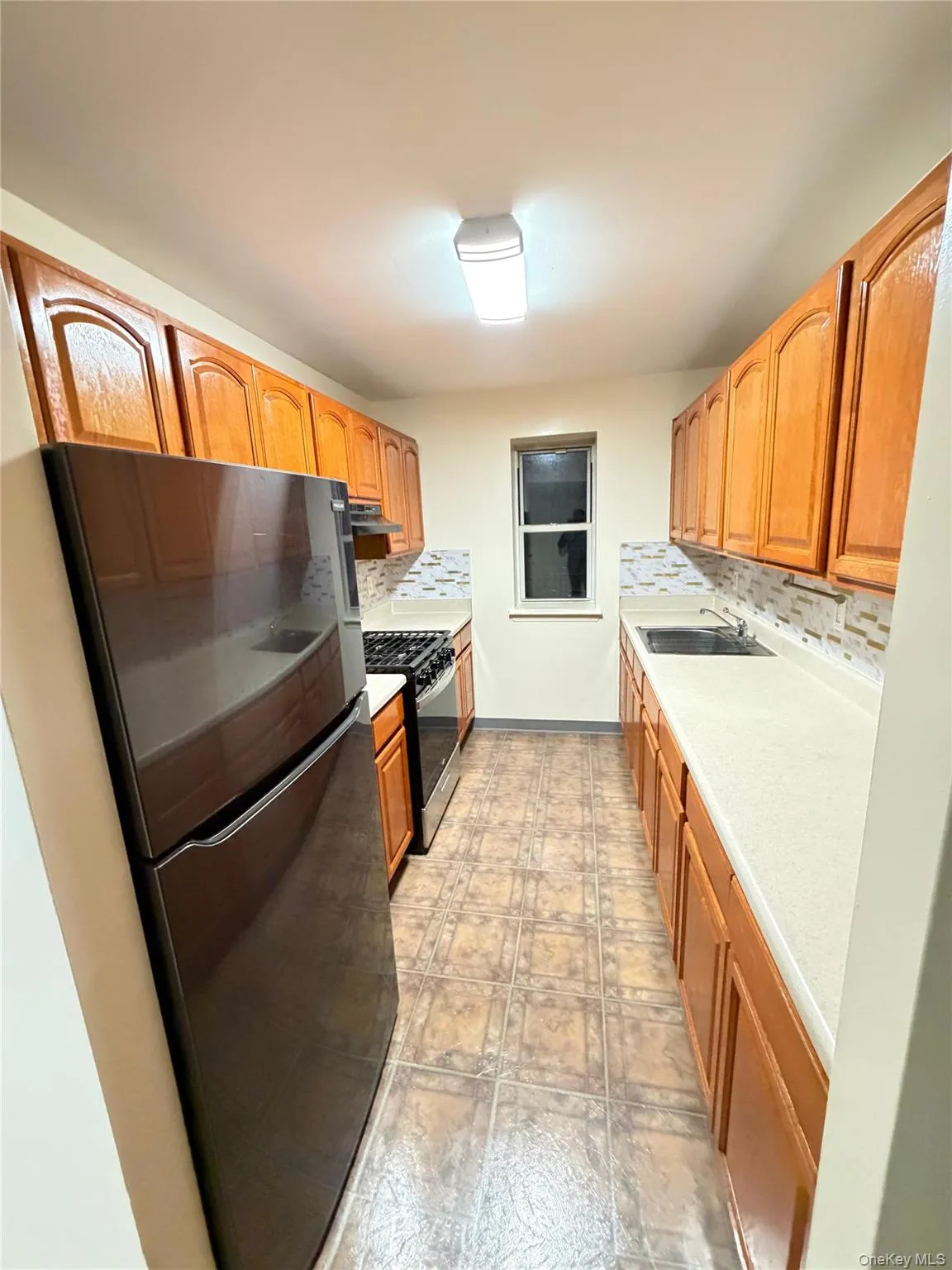 Galley kitchen featuring wood-finish cabinetry, light countertops, and a full suite of appliances Galley kitchen featuring wood-finish cabinetry, light countertops, and a full suite of appliances
