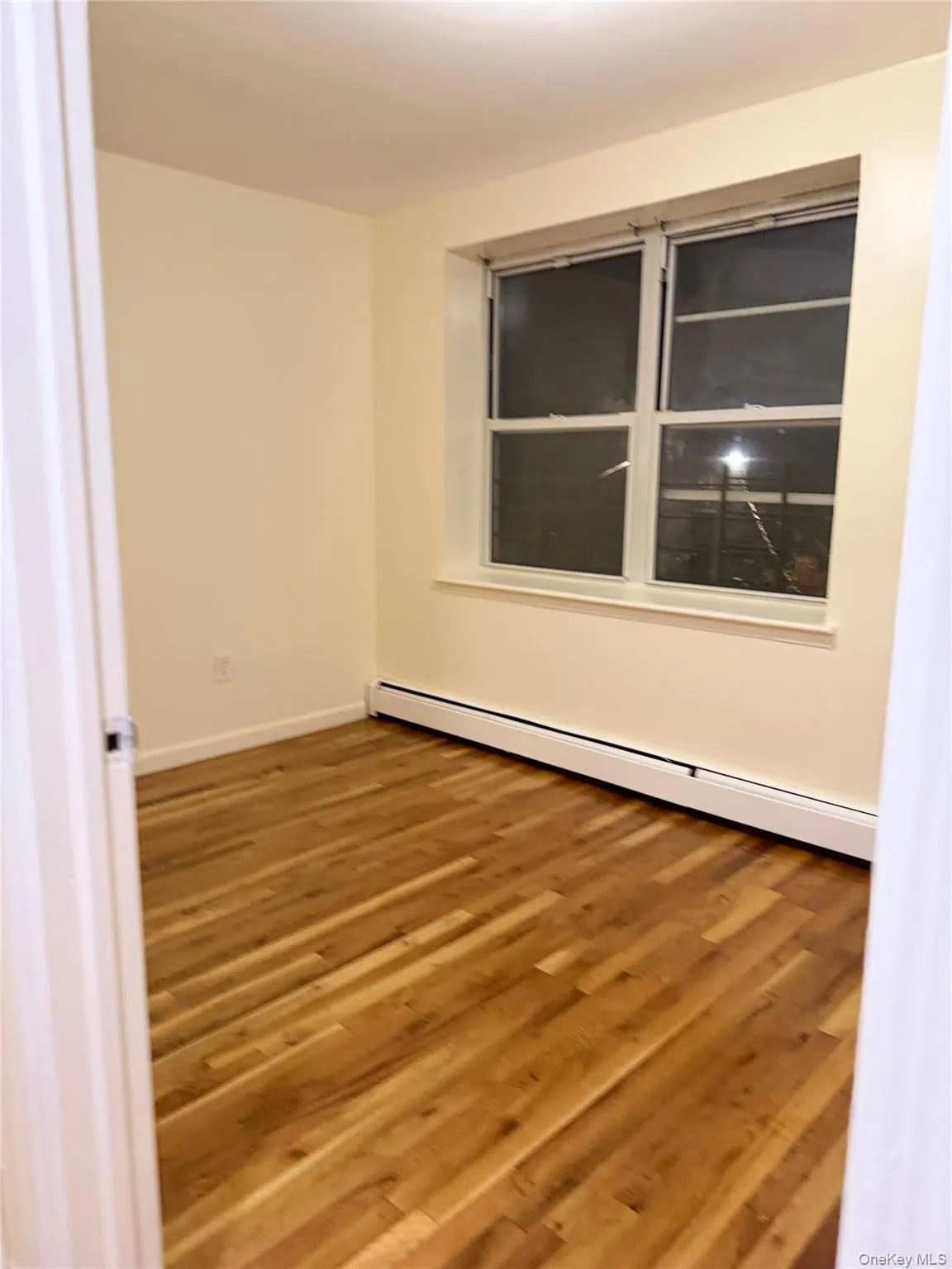 Room featuring wood-finish flooring, a double-paned window, and a baseboard heating unit Room featuring wood-finish flooring, a double-paned window, and a baseboard heating unit