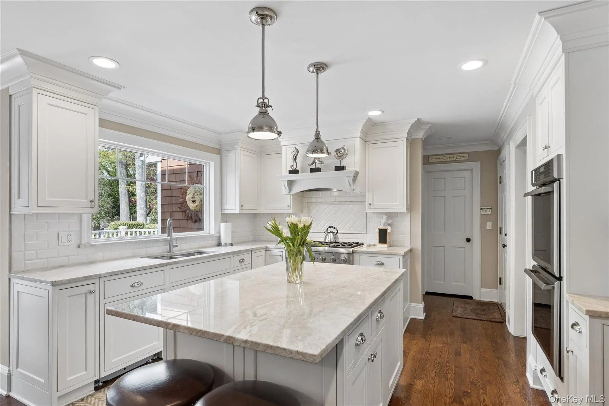 Open-concept eat -kitchen featuring hardwood flooring, white cabinetry, a center island with quartzite countertop and top tier stainless steel appliances Open-concept eat -kitchen featuring hardwood flooring, white cabinetry, a center island with quartzite countertop and top tier stainless steel appliances