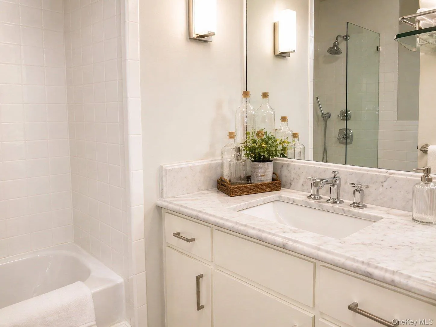 Full bath with white vanity, marble-style surfaces and glass-enclosed bathing area. Full bath with white vanity, marble-style surfaces and glass-enclosed bathing area.