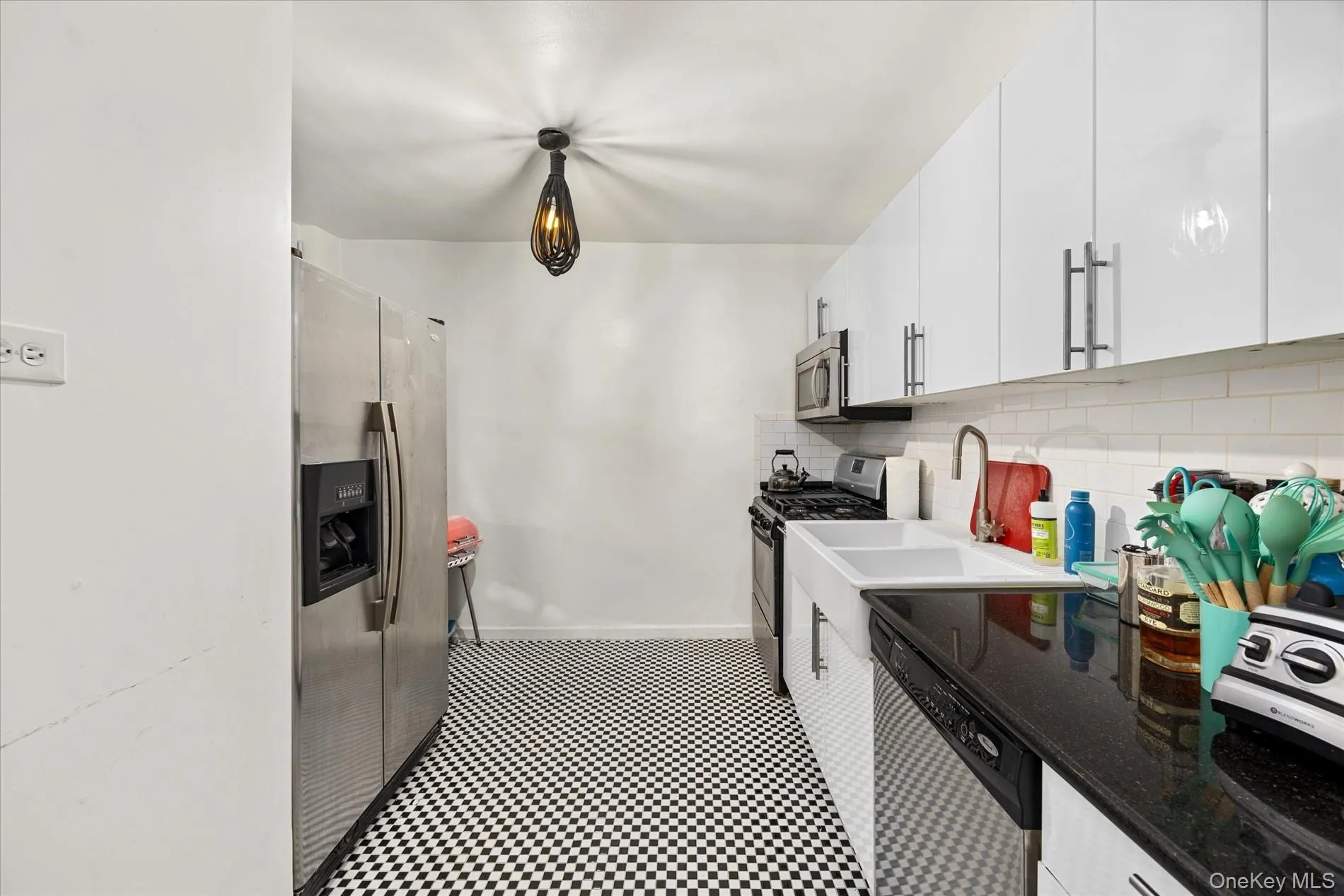 Kitchen featuring a stainless steel side-by-side refrigerator, white upper cabinetry, black countertops, and a white subway tile backsplash Kitchen featuring a stainless steel side-by-side refrigerator, white upper cabinetry, black countertops, and a white subway tile backsplash