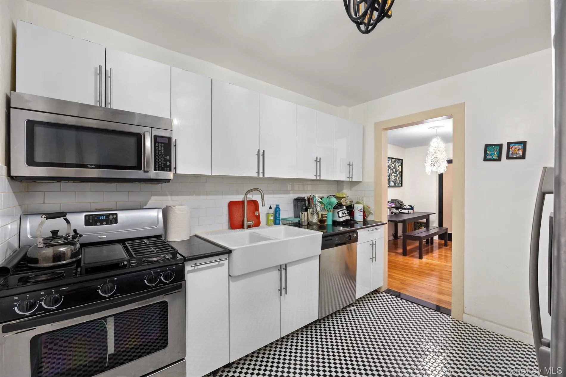 Kitchen featuring checkerboard flooring, white subway tile backsplash, white shaker-style cabinetry, stainless steel appliances, and a farmhouse sink Kitchen featuring checkerboard flooring, white subway tile backsplash, white shaker-style cabinetry, stainless steel appliances, and a farmhouse sink