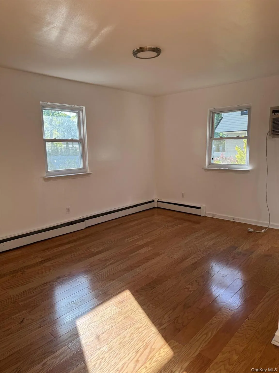 Hardwood flooring throughout featuring white baseboards, two windows, and a flush-mount ceiling light fixture Hardwood flooring throughout featuring white baseboards, two windows, and a flush-mount ceiling light fixture